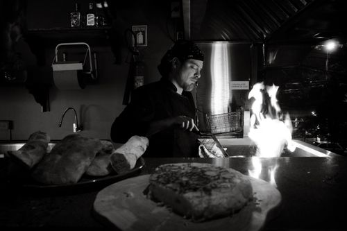 Free Black and white image of a chef preparing food with an open flame in a dimly lit kitchen. Stock Photo