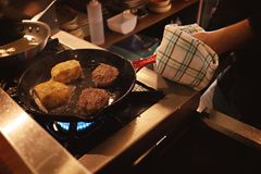 Close-up of two burgers and two patties cooking in a pan on a stove, kitchen scene.