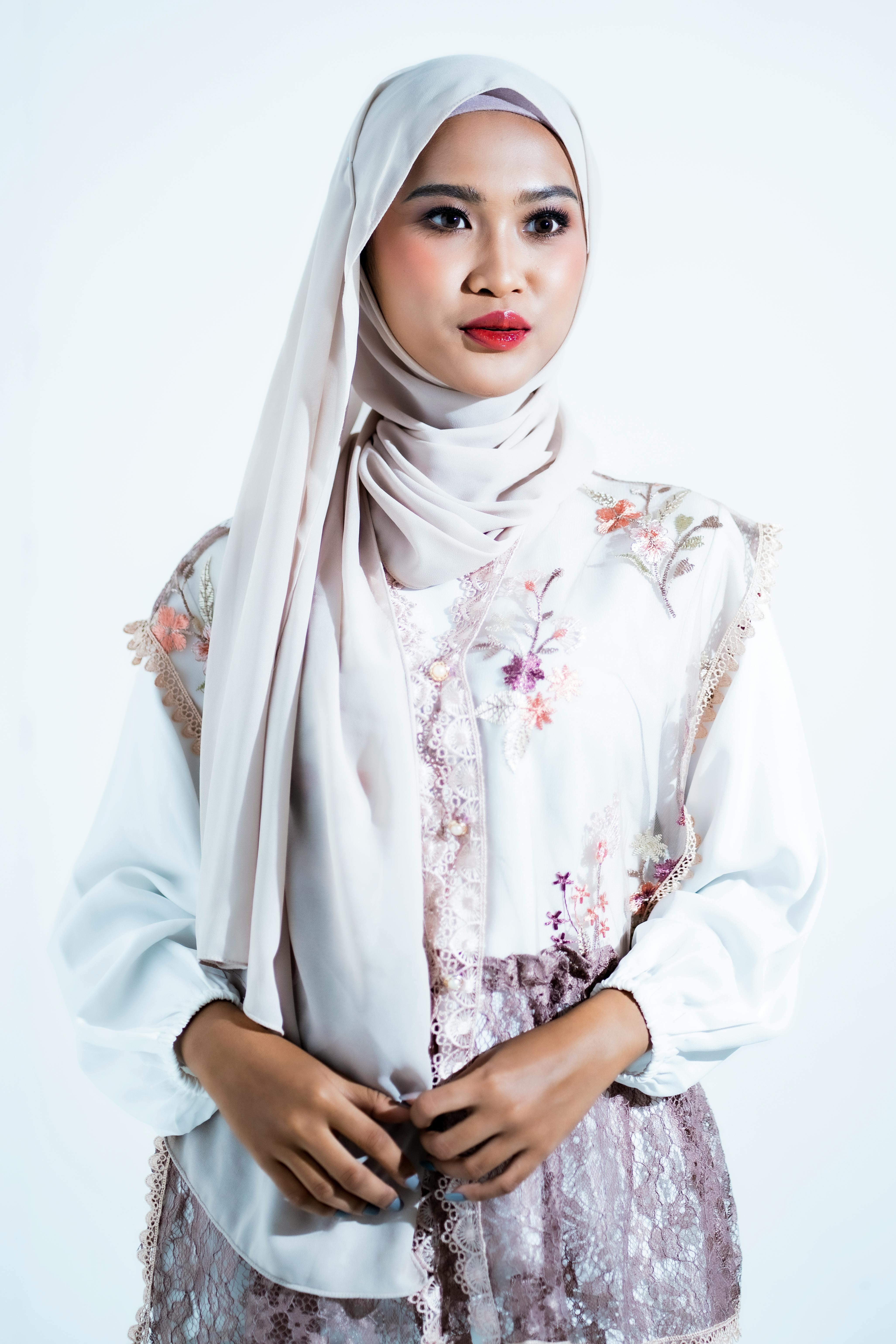 Gratis Elegante ritratto di una donna che indossa un leggero hijab floreale, che trasmette grazia e stile in uno studio. Foto a disposizione