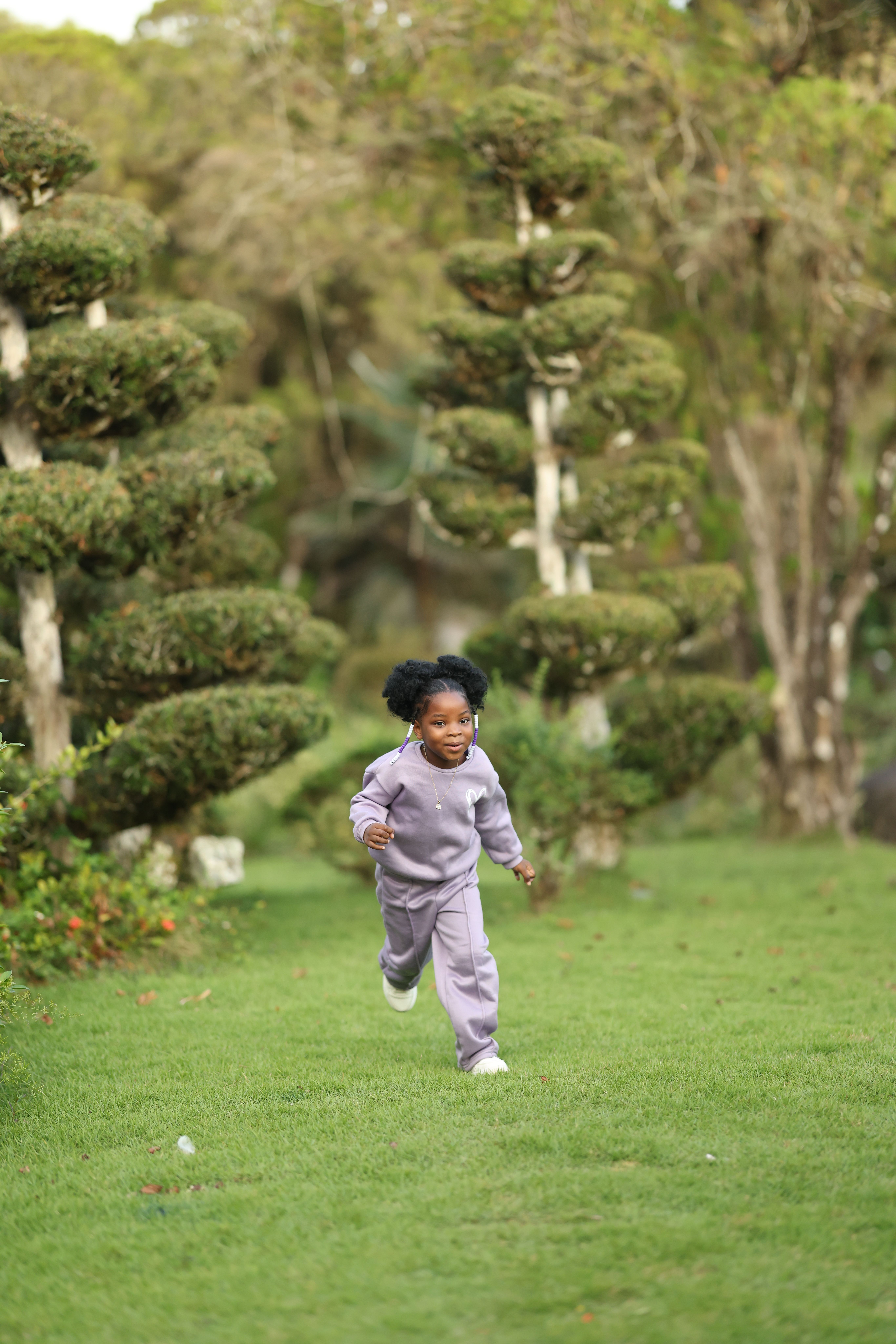 A happy young girl running through a lush green garden with neatly trimmed trees.