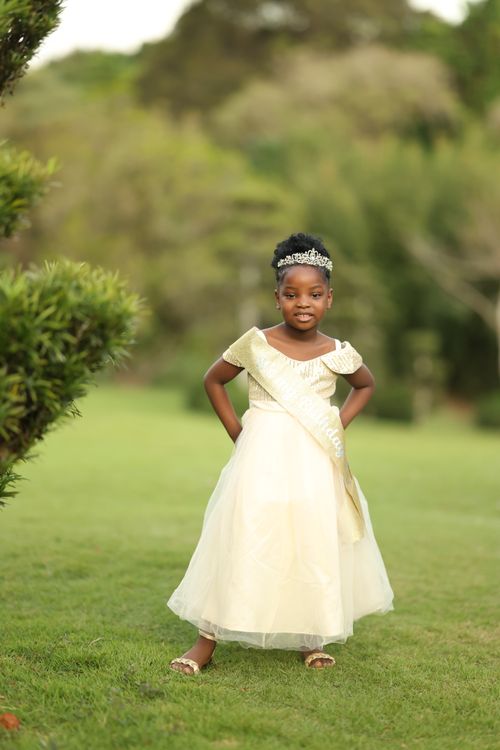 Free Charming black girl in a white princess dress with tiara posing outdoors in a garden. Stock Photo