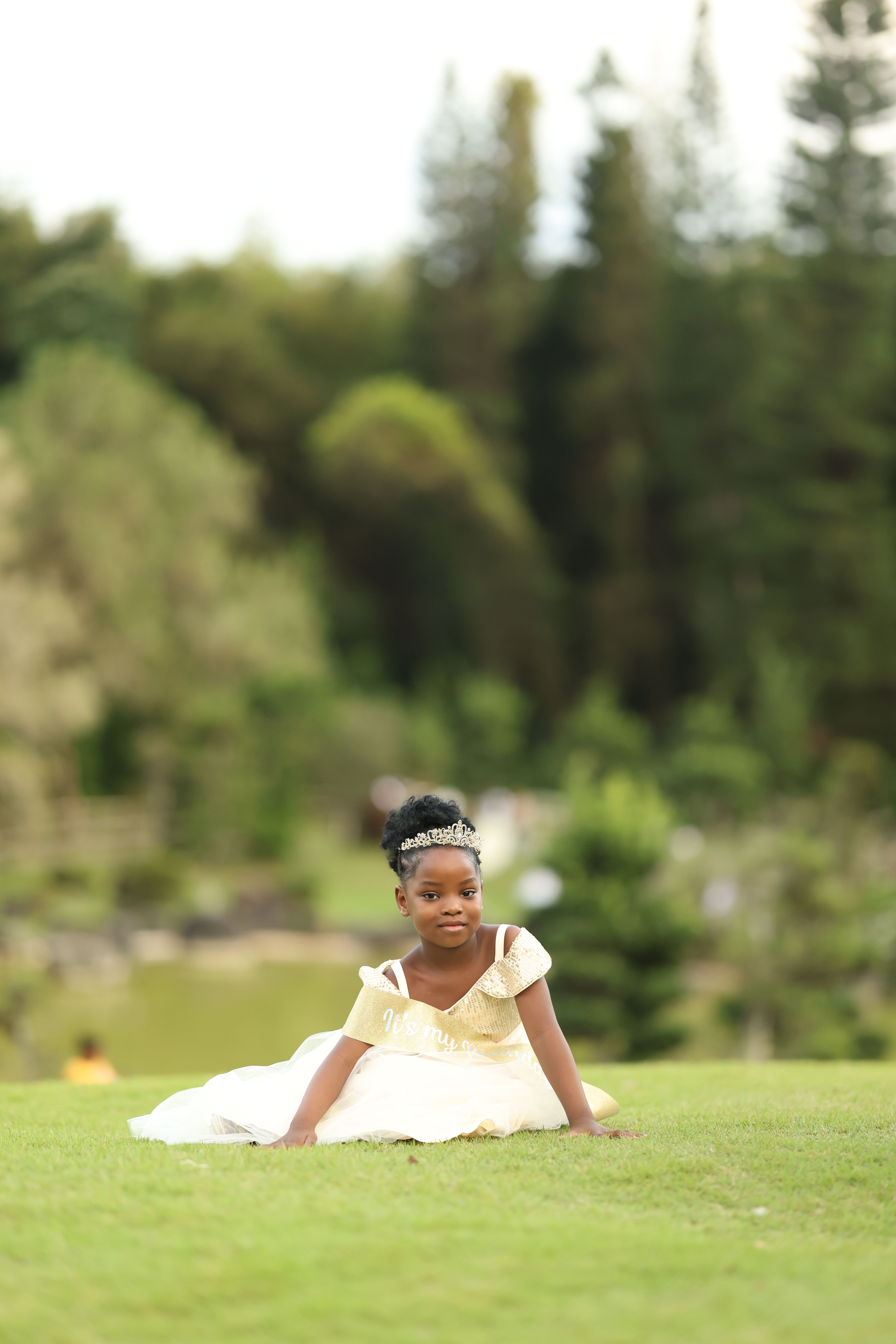 Adorable young girl sitting gracefully on grassy field, wearing a charming dress.