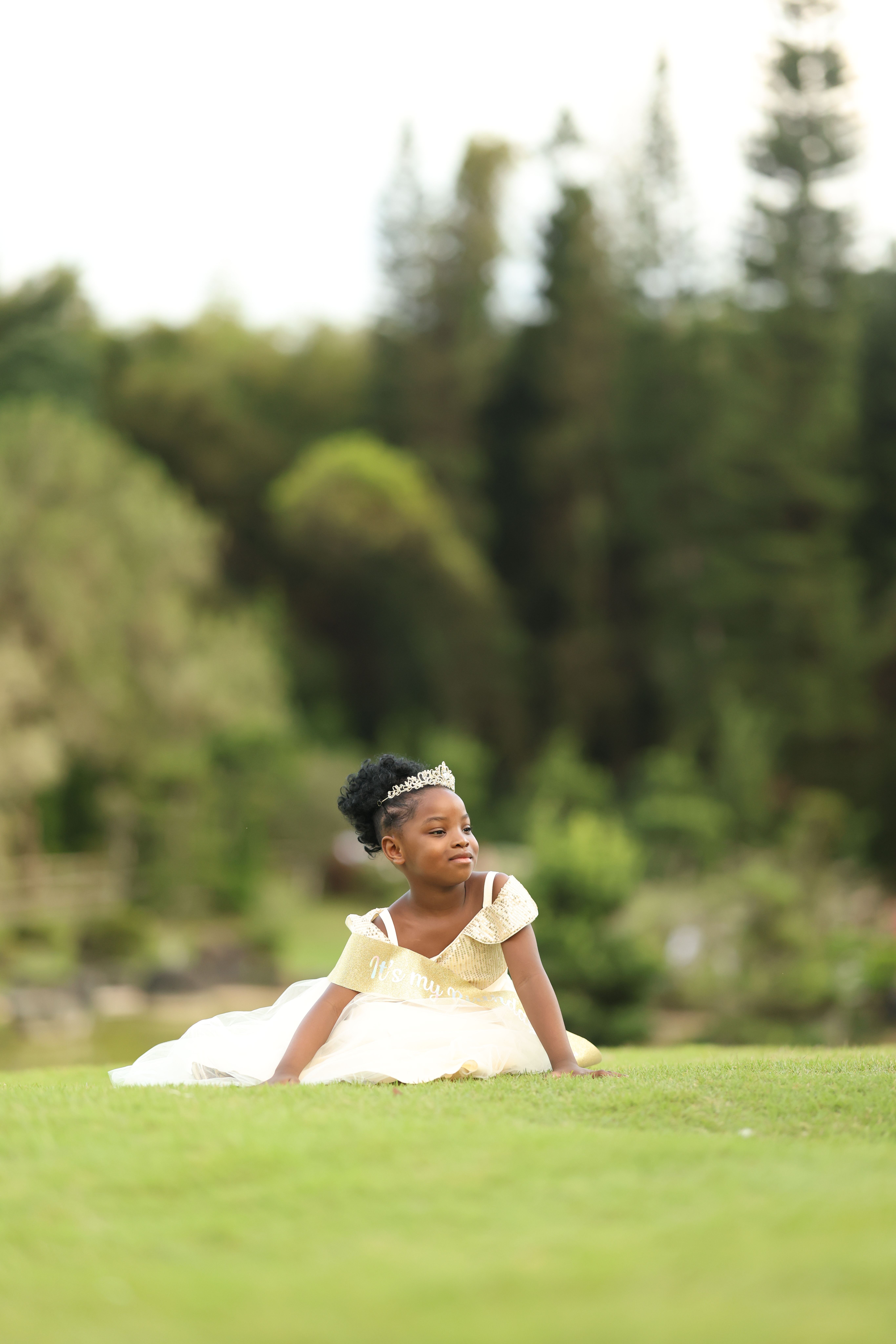 A young girl wearing a princess dress, lying on grass in a serene outdoor setting.