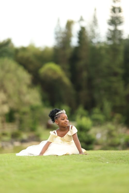 Free A young girl wearing a princess dress, lying on grass in a serene outdoor setting. Stock Photo