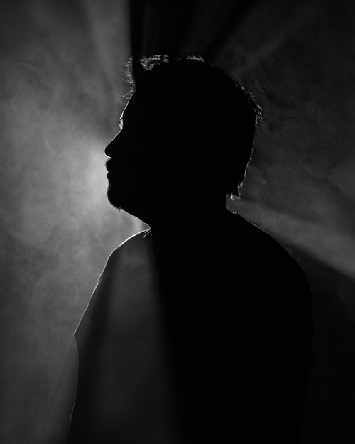 Free Black and white portrait of a man's silhouette with dramatic lighting creating a halo effect. Stock Photo