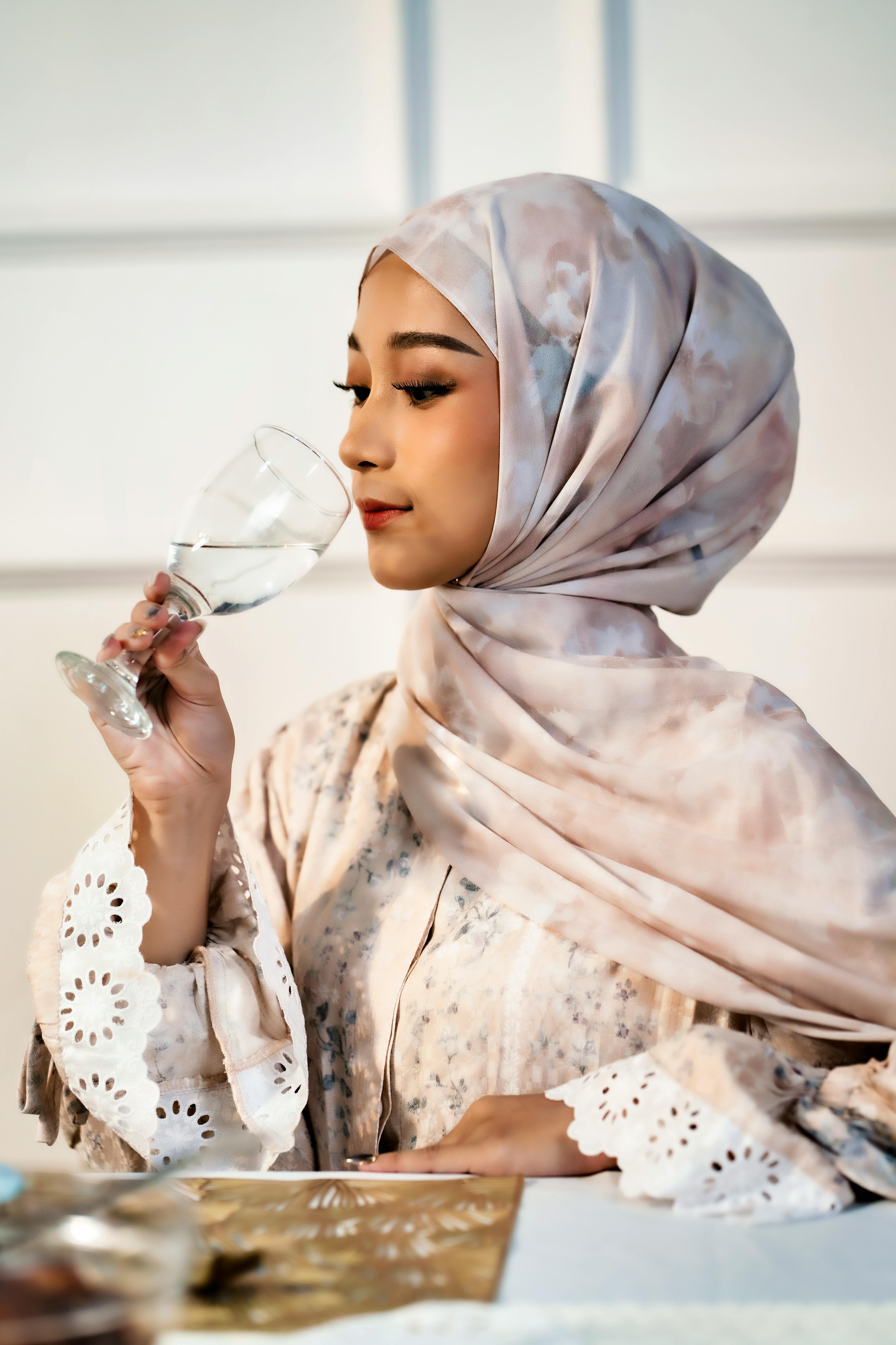 ingyenes Egy hidzsábot viselő fiatal nő derűs arckifejezéssel iszik egy pohárból bent. Stockfotó