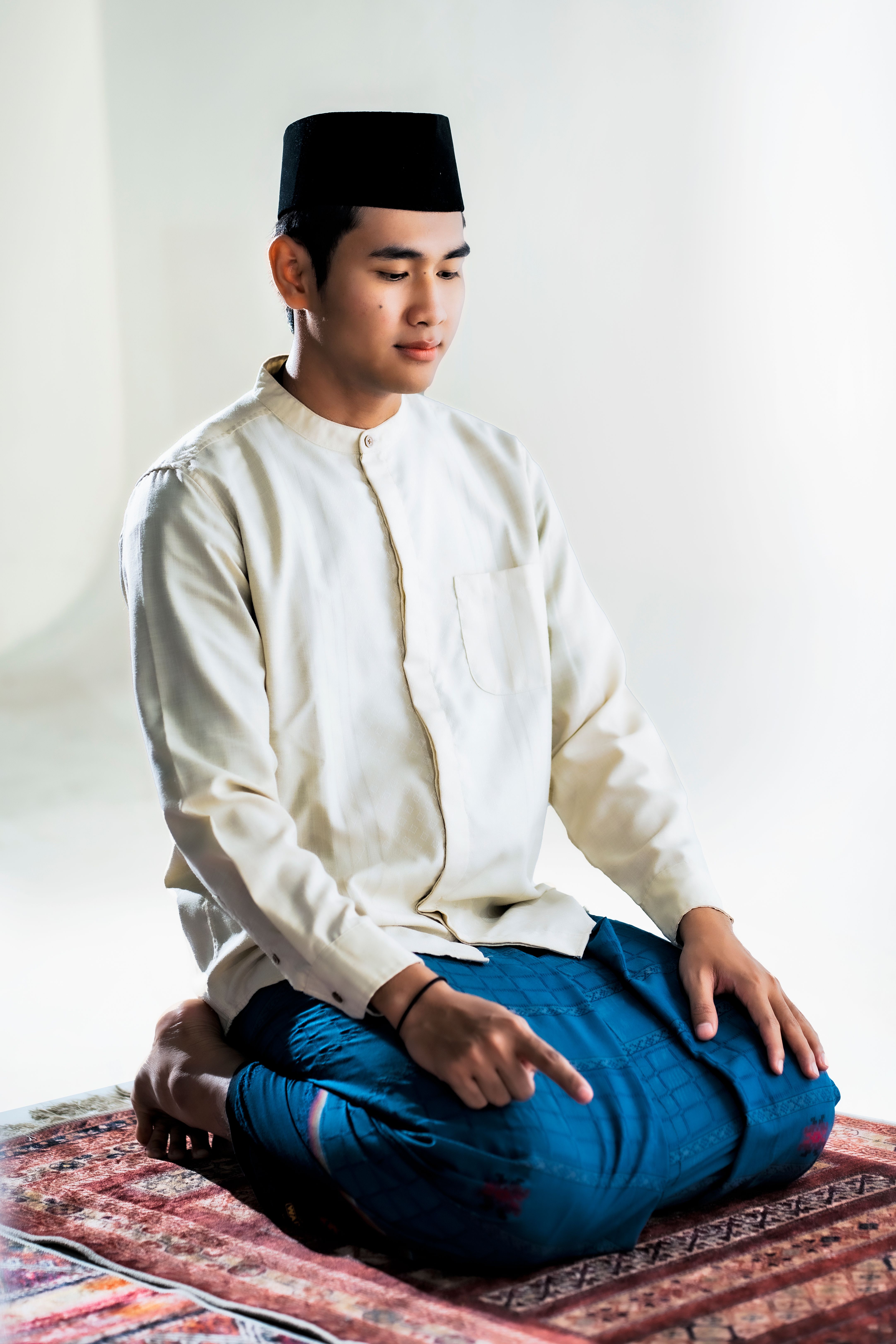 Portrait of a young man in traditional attire meditating in a peaceful indoor setting.