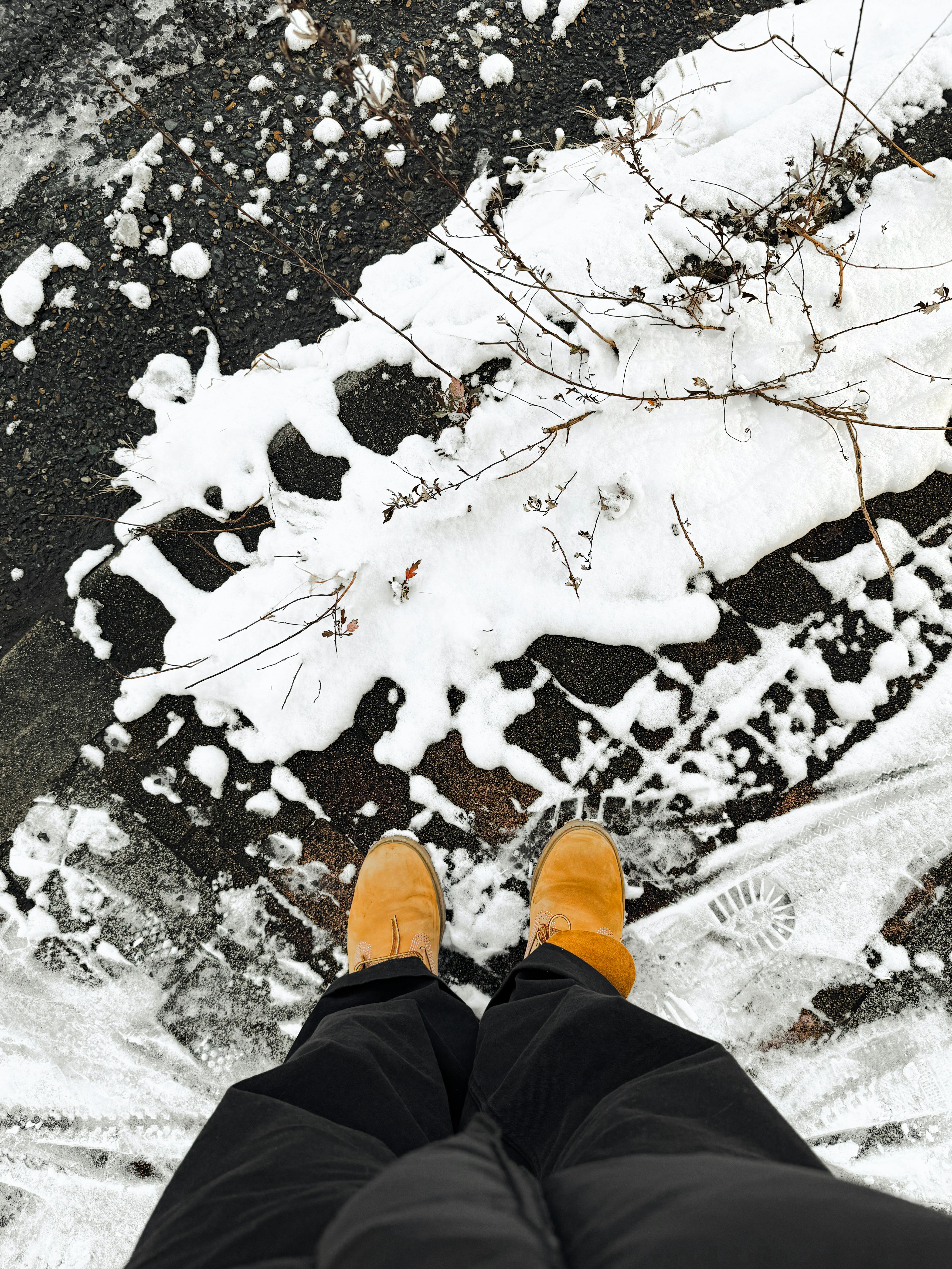 Miễn phí Một người đàn ông đứng trên vỉa hè phủ đầy tuyết, đi đôi ủng màu vàng, ghi lại trọn vẹn vẻ đẹp của mùa đông. Ảnh lưu trữ