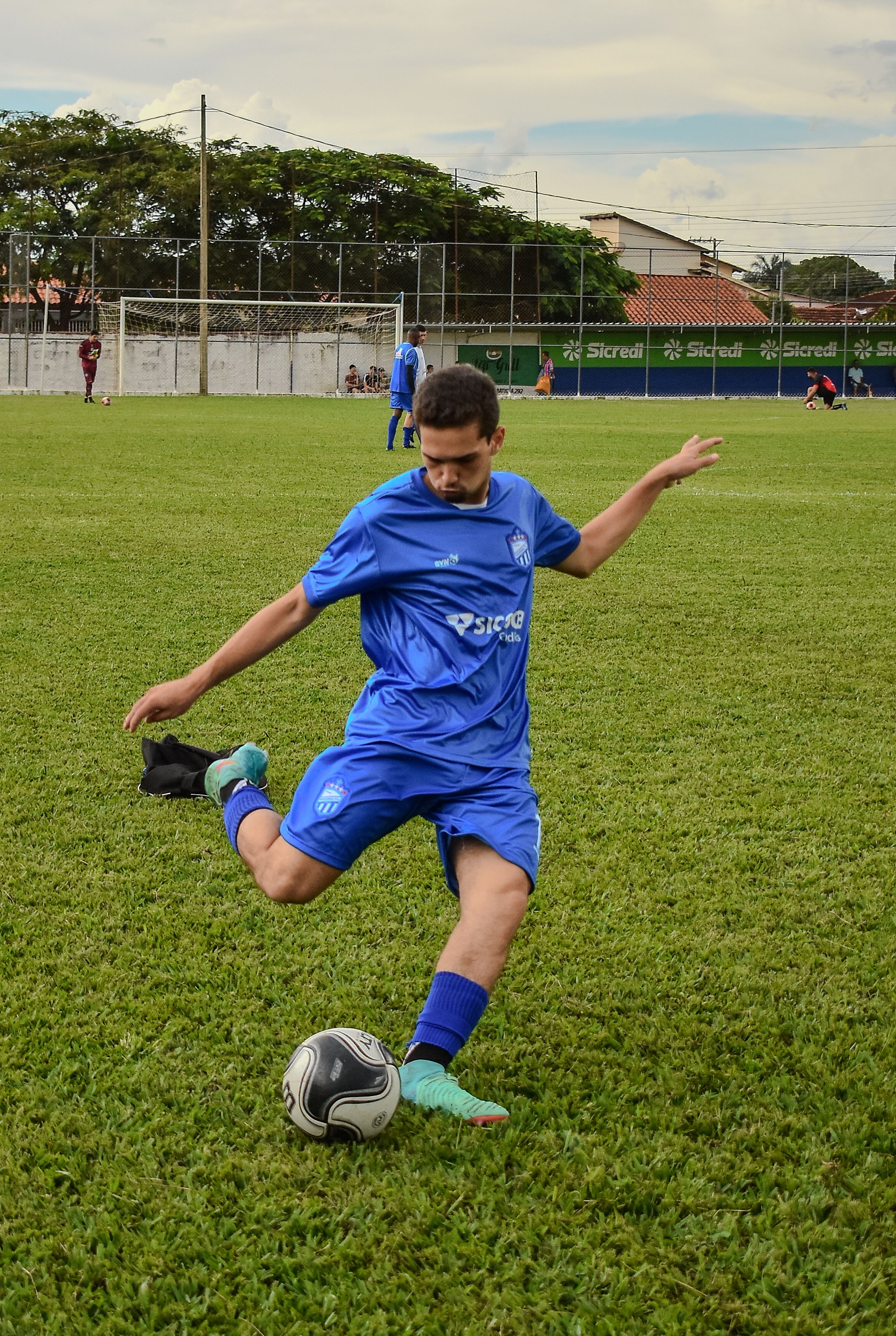A young soccer player in blue uniform skillfully kicks the ball during a match.