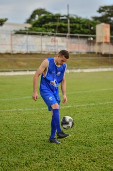 A young male soccer player in blue uniform practicing ball control on a grass field.