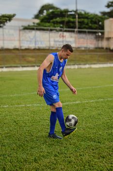 A young soccer player in a blue uniform practicing with a soccer ball on an outdoor field.