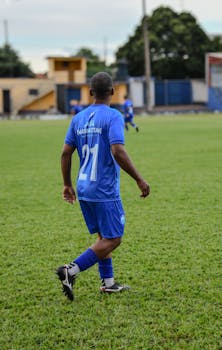 A soccer player wearing a blue jersey walks on a grass field during a match.