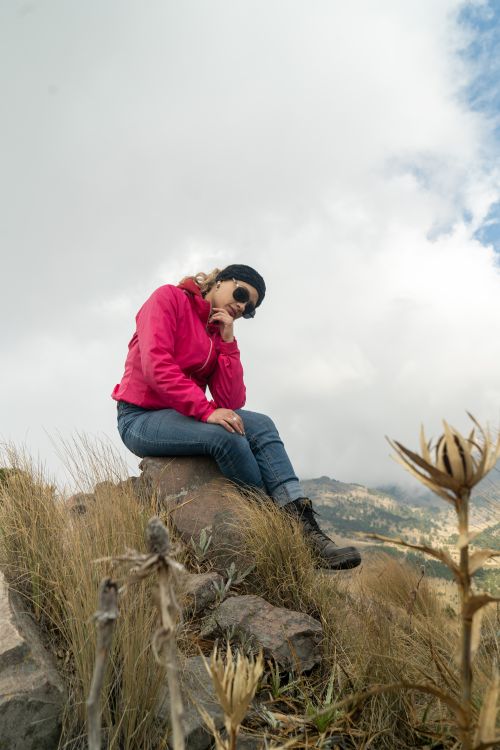 Free Woman in pink jacket sitting on a rock, enjoying mountain view. Stock Photo
