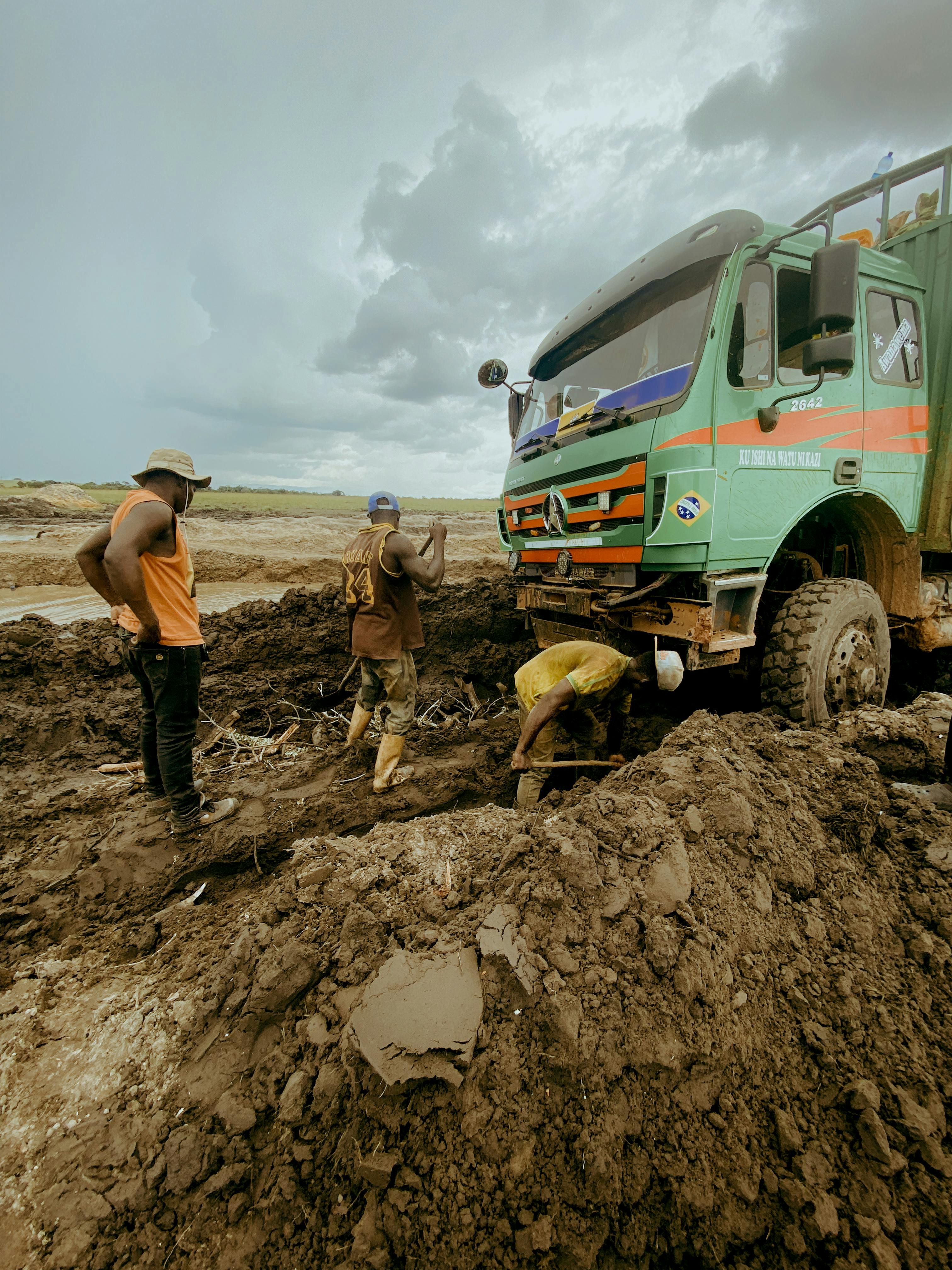 Miễn phí Các công nhân nỗ lực giải cứu một chiếc xe tải bị mắc kẹt trong địa hình lầy lội dưới bầu trời nhiều mây, thể hiện tinh thần đồng đội và sự kiên trì. Ảnh lưu trữ