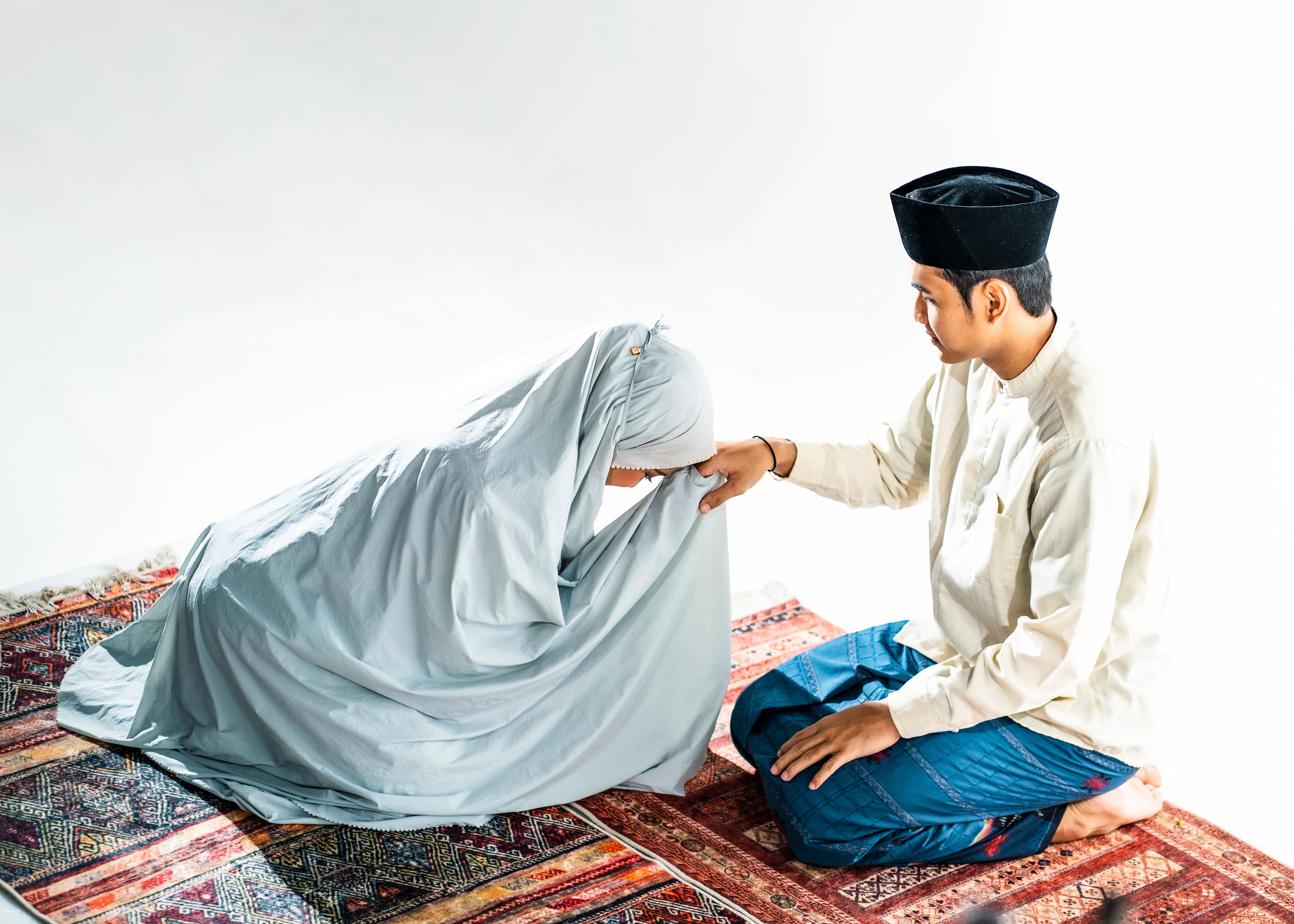 A Muslim man and woman praying on a traditional rug, signifying devotion and spirituality.