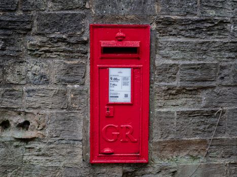 Classic red GR postbox set against a stone wall in Ripon, UK.