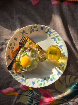 Fried egg on toast served on a decorative plate with herbal tea, captured in natural light.