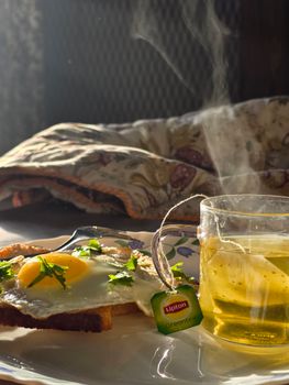 Enjoy a warm breakfast with fried eggs on toast and a steaming cup of green tea.