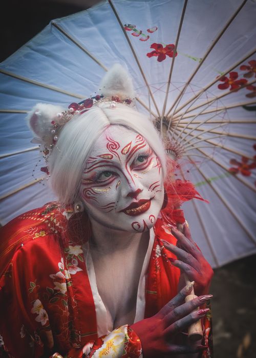 Free A person in vibrant geisha cosplay with elaborate makeup and red kimono. Stock Photo