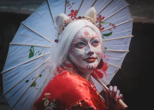 Free Culturally inspired portrait in geisha-style face paint holding a decorative parasol. Stock Photo