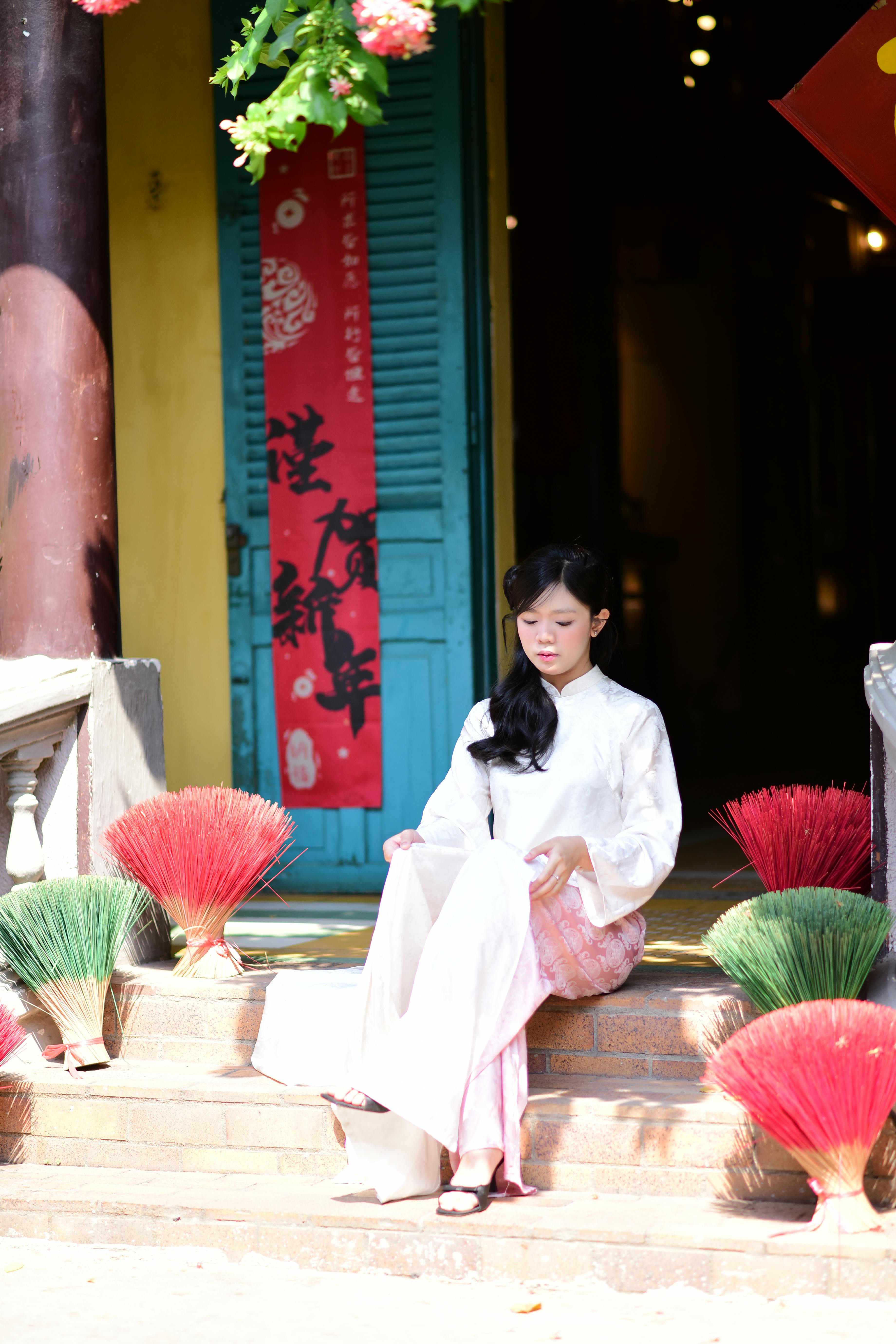 Gratis En kvinne i tradisjonell drakt sitter fredelig utenfor en butikk med fargerike røkelsespinner. Arkivbilde