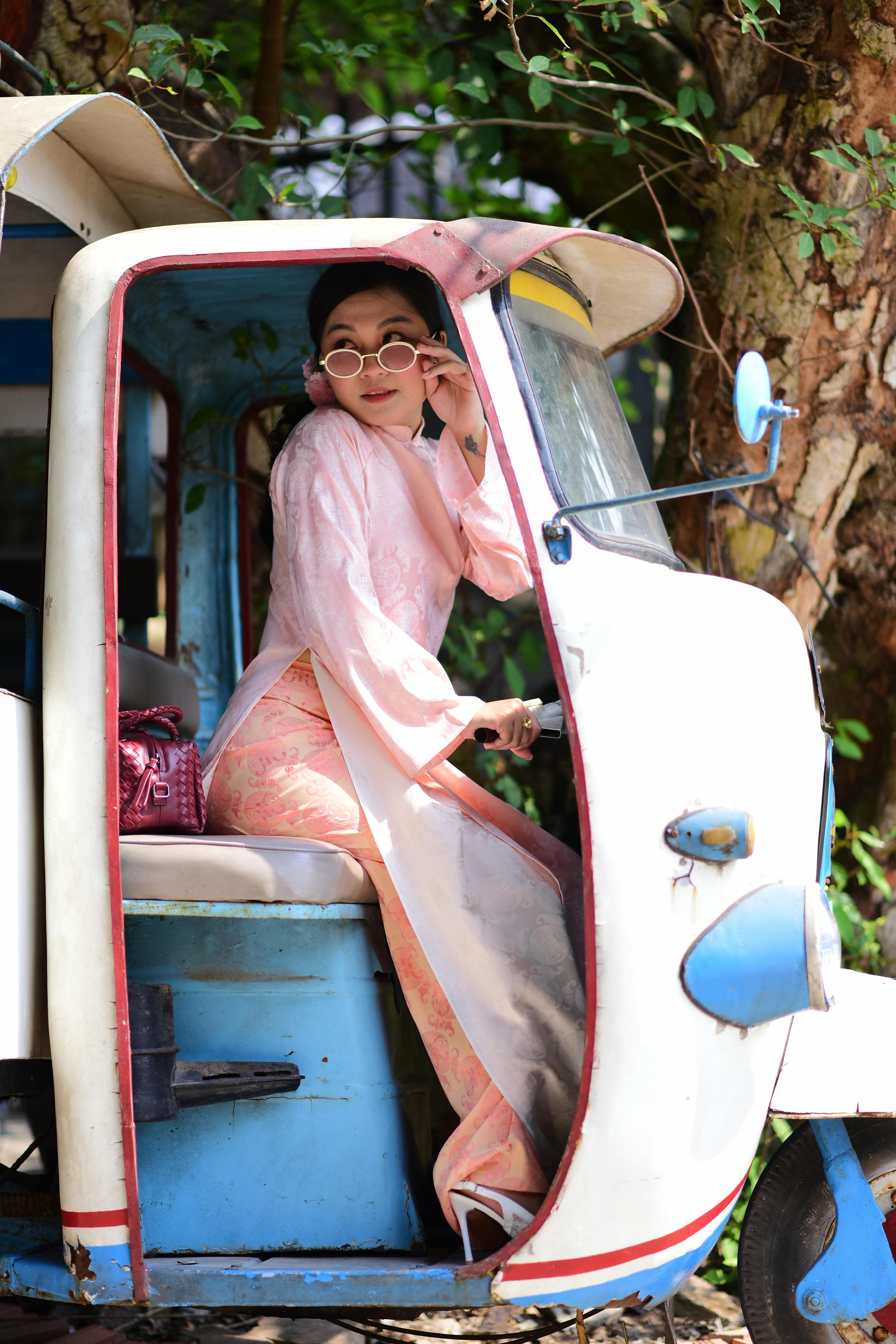 ฟรี หญิงสาวผู้สง่างามในชุดพื้นเมืองสีชมพูกำลังโพสท่าอยู่บนรถตุ๊กตุ๊กโบราณในสถานที่กลางแจ้ง คลังภาพถ่าย