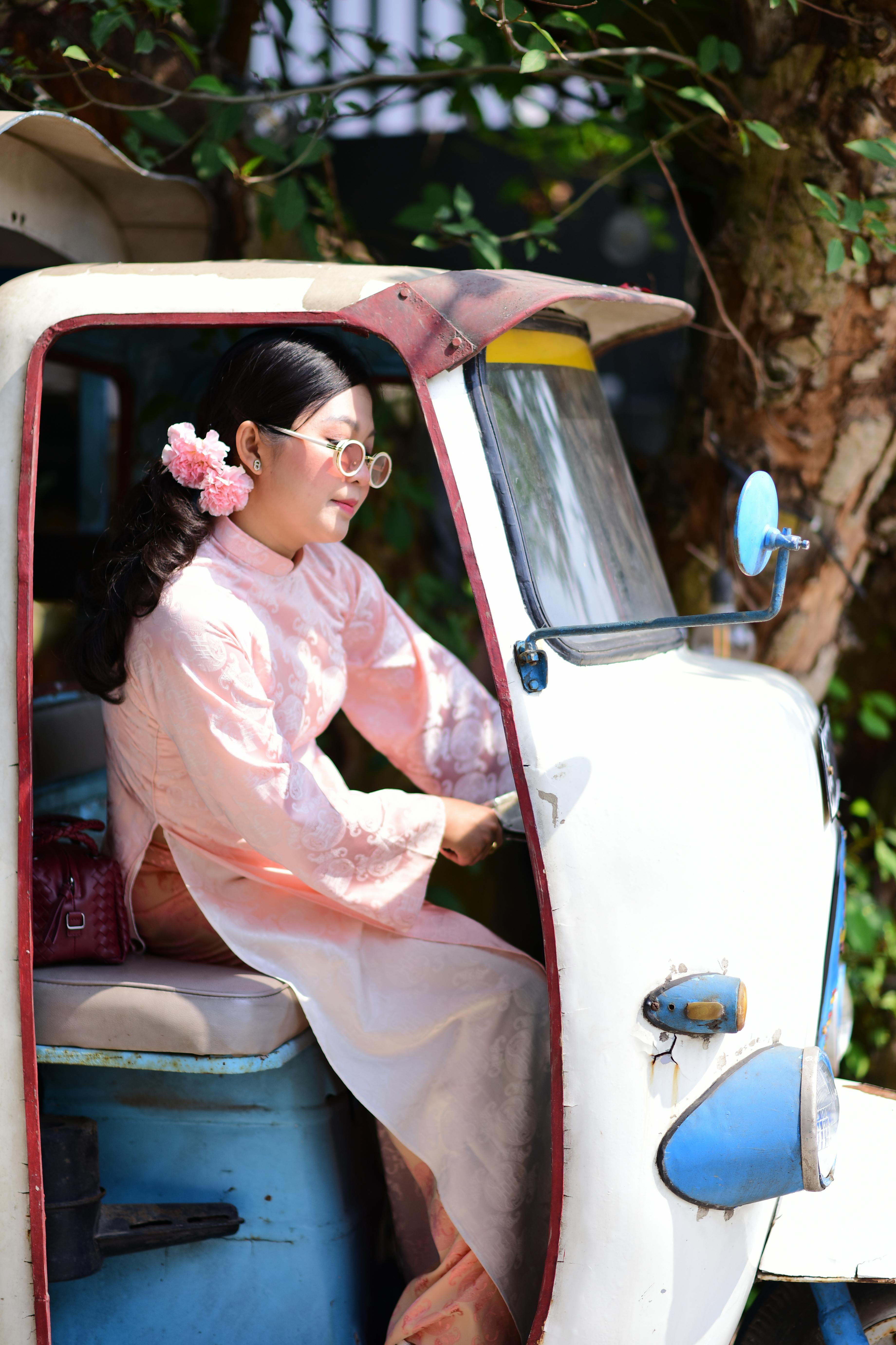 ingyenes Rózsaszín ao dai-ban ülő ázsiai nő egy tuk-tukban élvezi a napsütéses napot a szabadban. Stockfotó