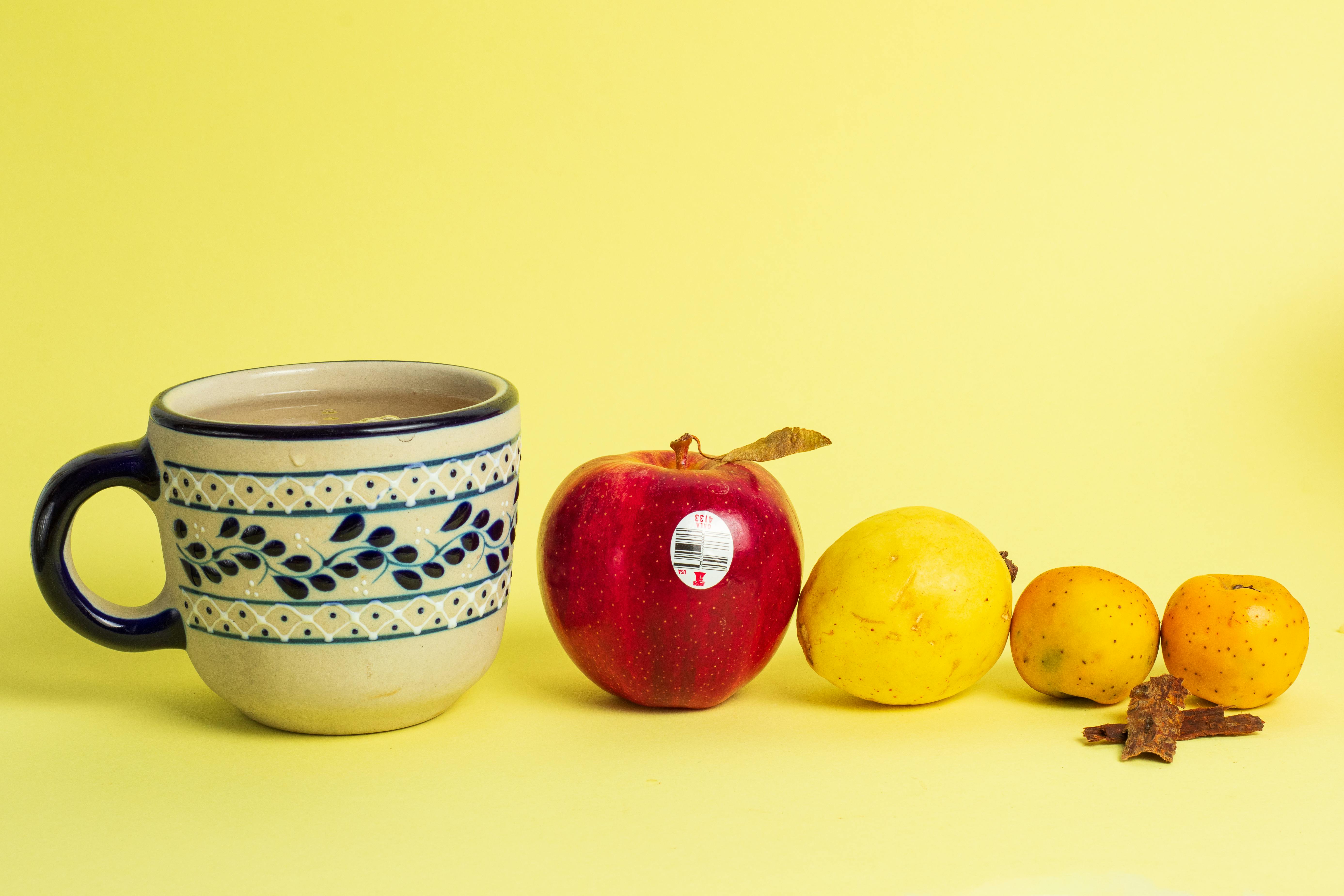 Gratis Natura morta colorata con tazza di ceramica, mela e frutta assortita su sfondo giallo. Foto a disposizione