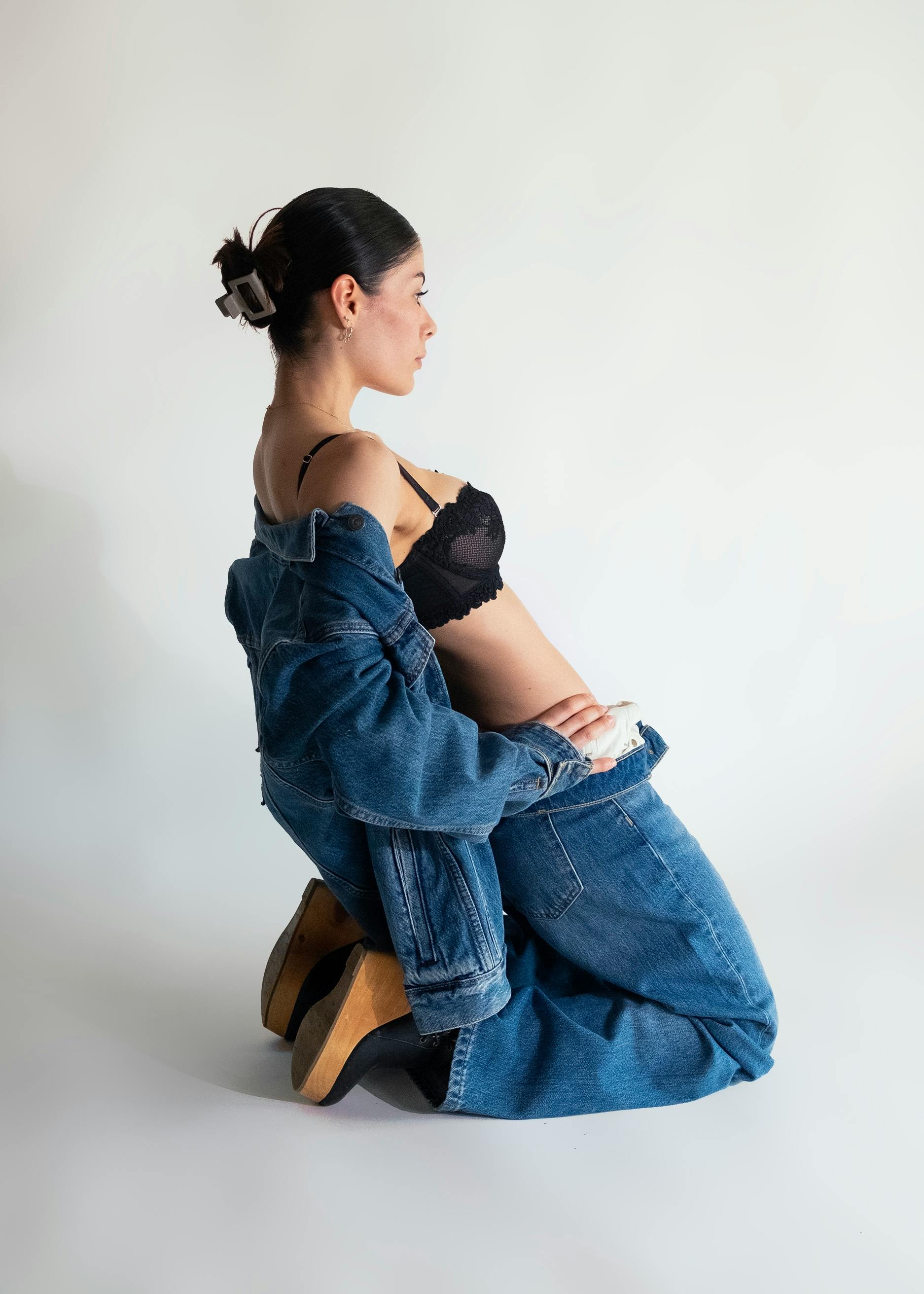 gratis Een stijlvolle vrouw in een spijkerjasje en zwarte lingerie knielt neer en toont mode en stijl. Stockfoto