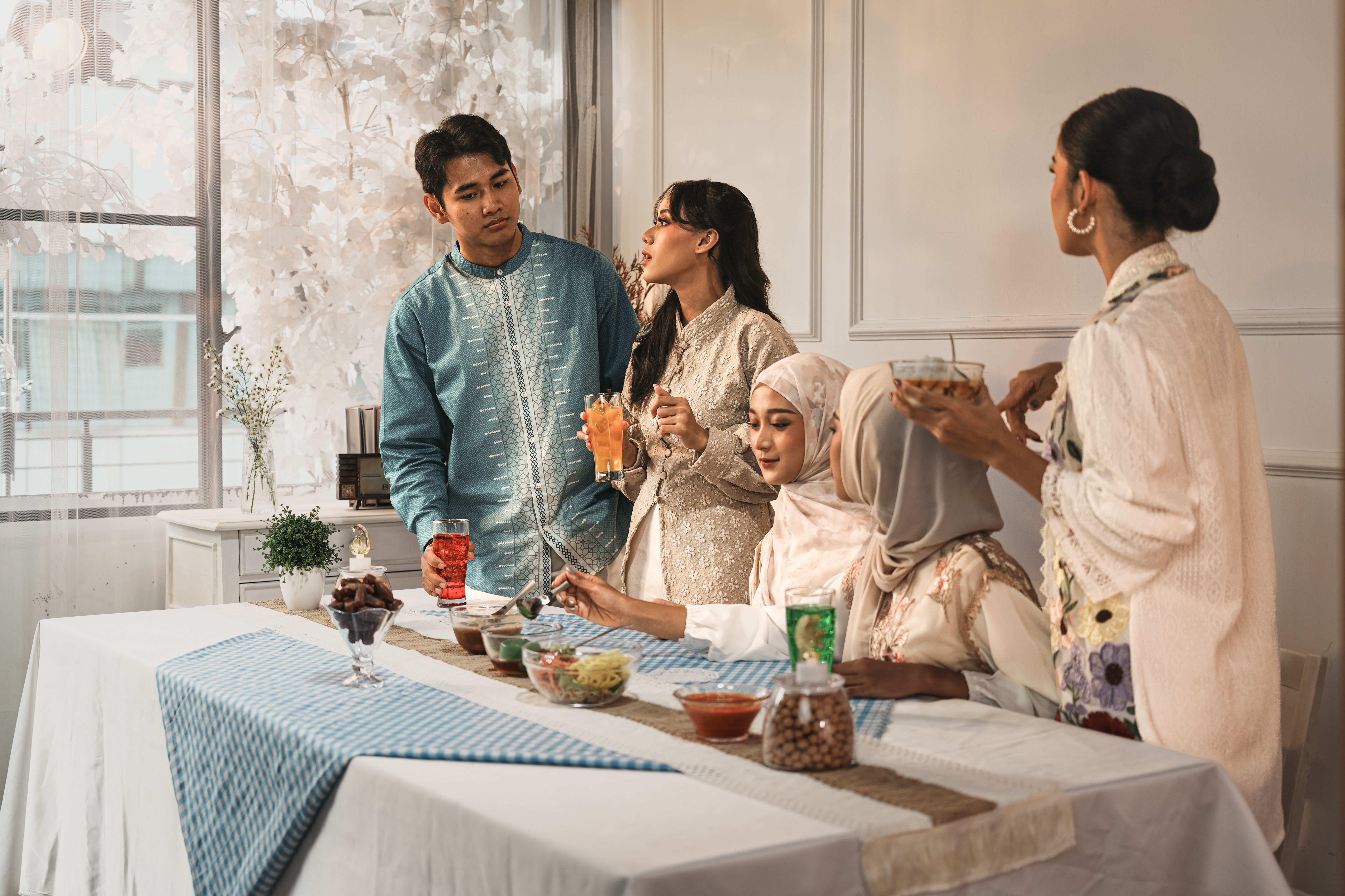 A diverse group sharing a meal indoors, dressed in elegant traditional attire, enjoying beverages and snacks.