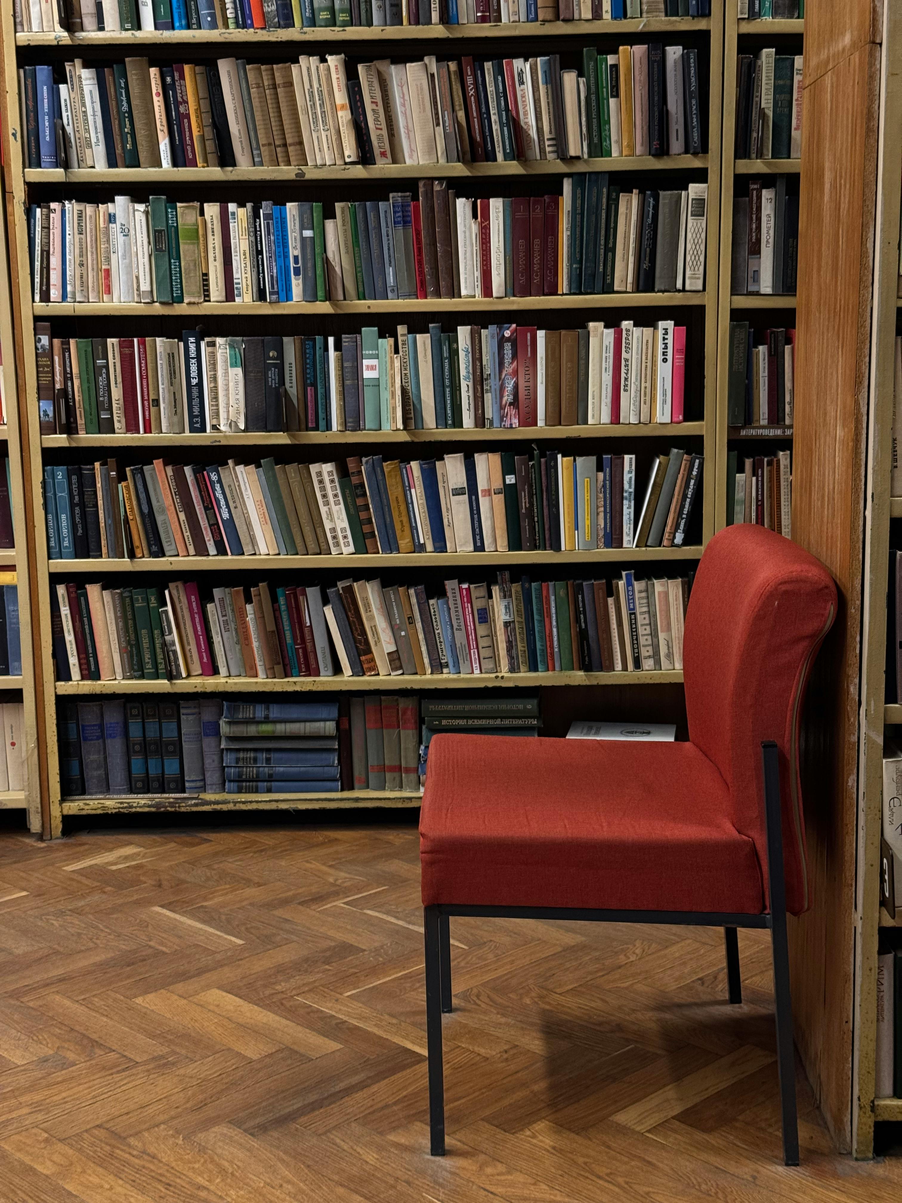 ingyenes Egy nyugodt könyvtári jelenet egy piros székkel, hátterében könyvespolcokkal. Stockfotó