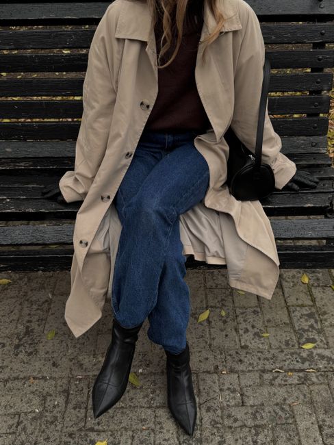 Woman in stylish autumn outfit sitting on a park bench, showcasing seasonal fashion trends.