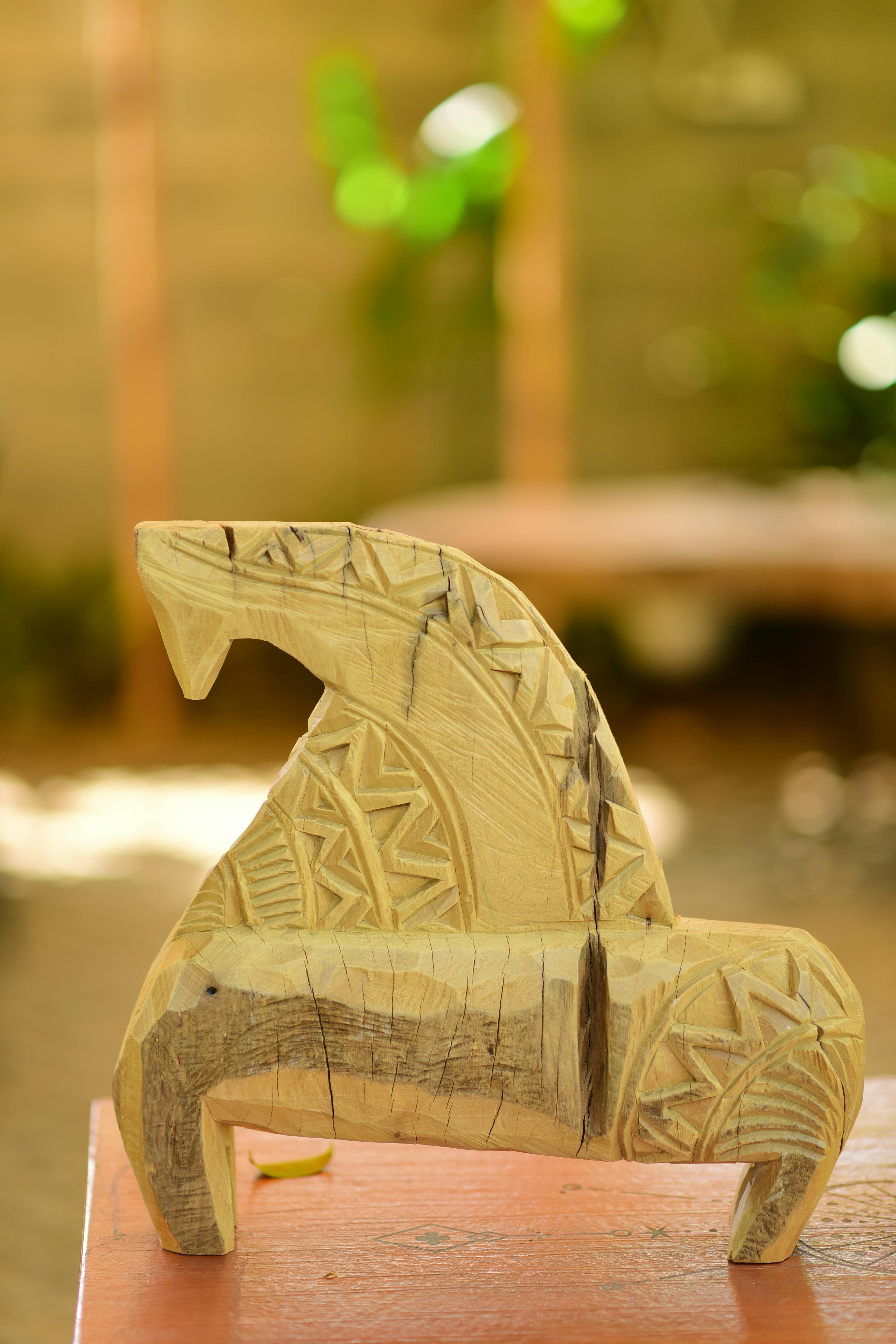 免费 一尊雕刻精美的木马雕像，饰有几何图案，摆放在户外的木桌上。 素材图片
