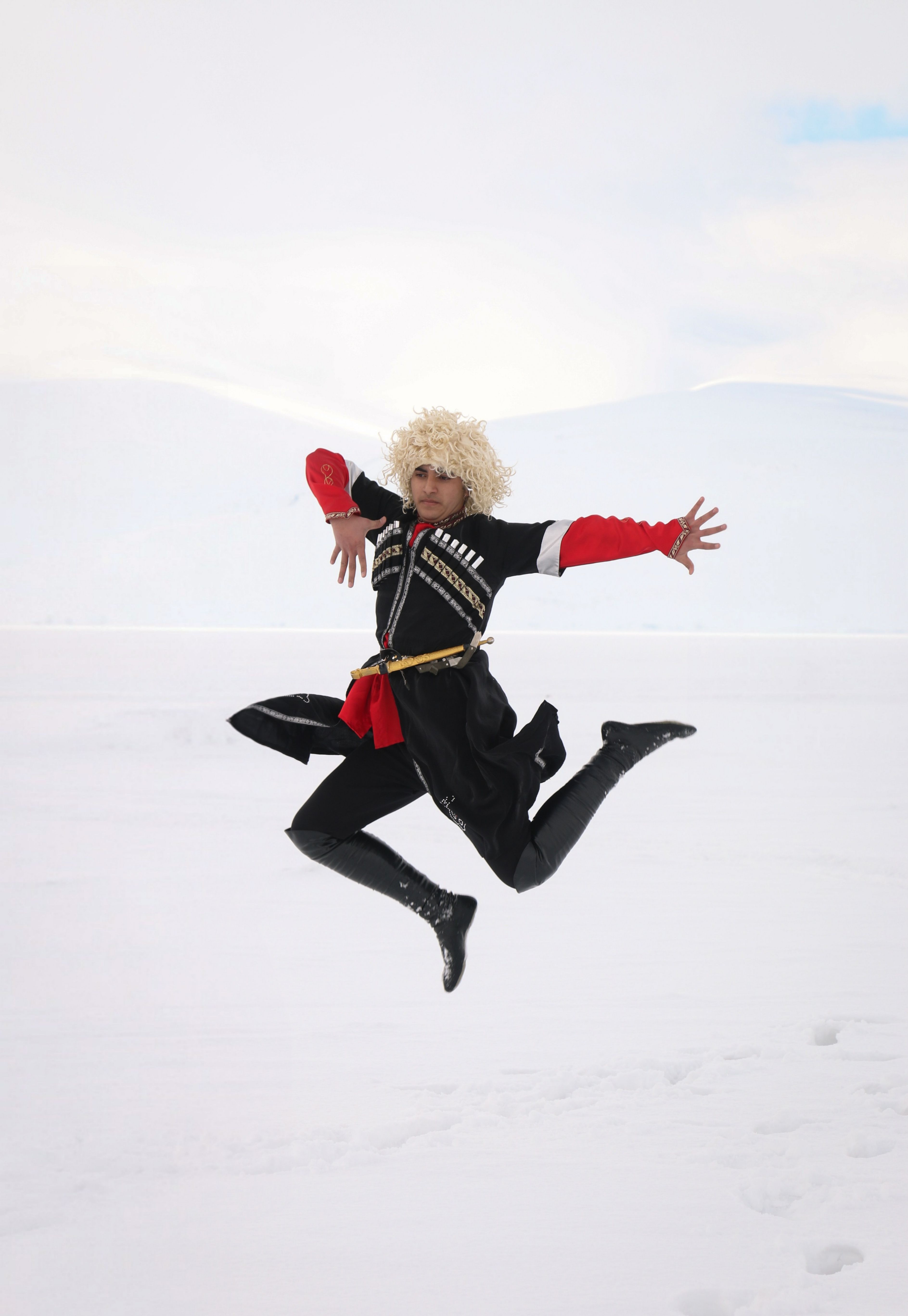 Dynamic shot of a Caucasian dancer leaping in traditional attire against a snowy backdrop in Kars, Türkiye.