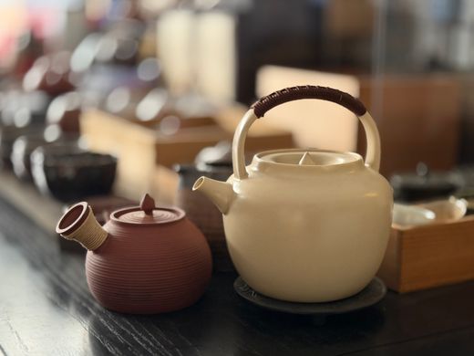 Cream ceramic teapot with wrapped handle beside a small clay teapot