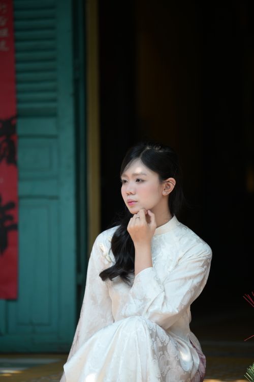 Free Young woman in elegant traditional Asian attire sitting thoughtfully indoors, exuding grace and serenity. Stock Photo