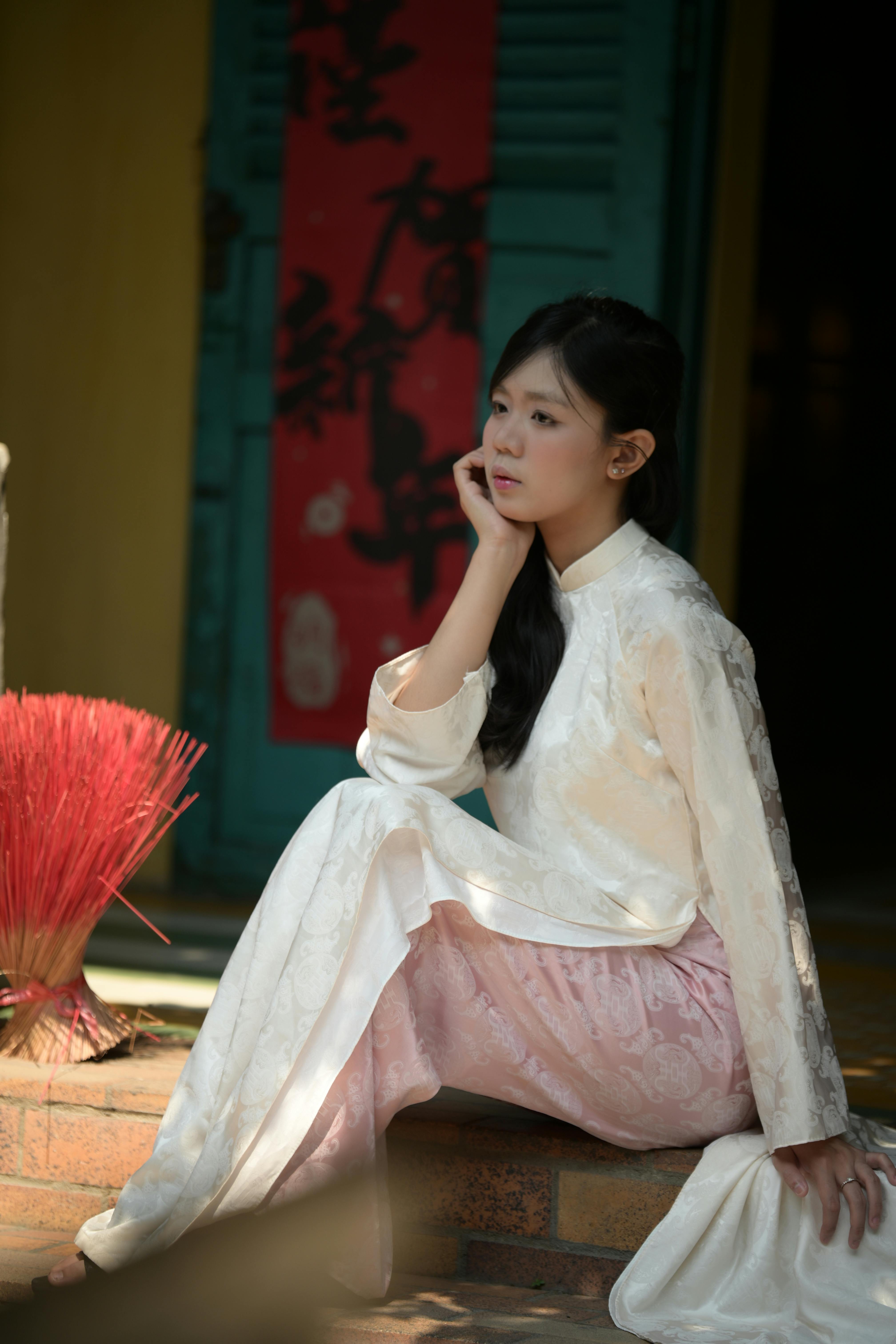 Free Thoughtful young woman in traditional attire sits near colorful backdrop. Stock Photo