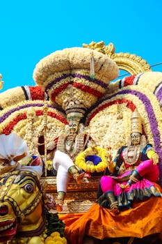 Colorful Indian festival parade showcasing traditional floral and deity decorations under a clear blue sky.