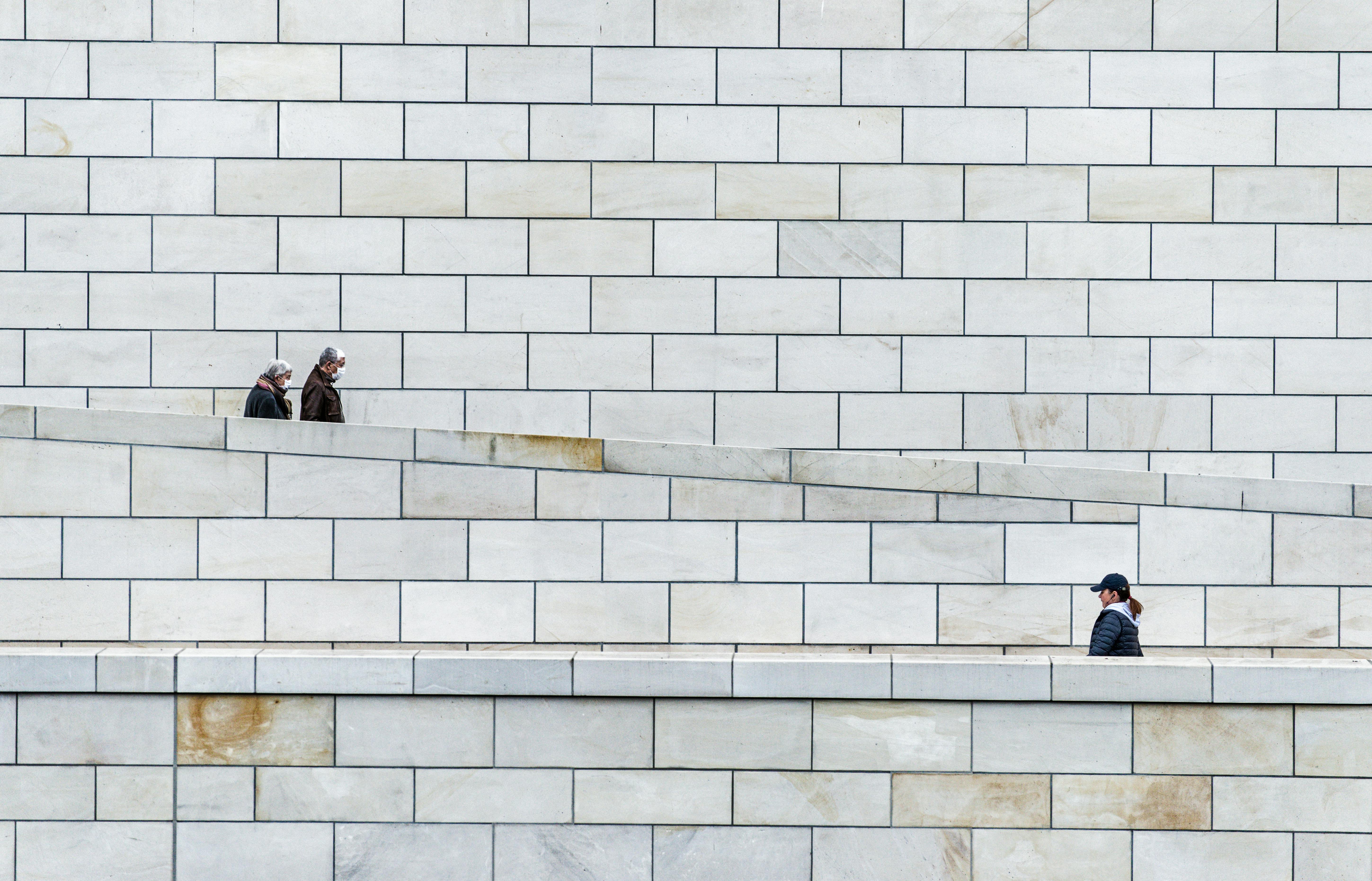 Gratis Escena urbana minimalista con tres personas en una rampa de hormigón contra una pared de ladrillo blanco. Foto de stock