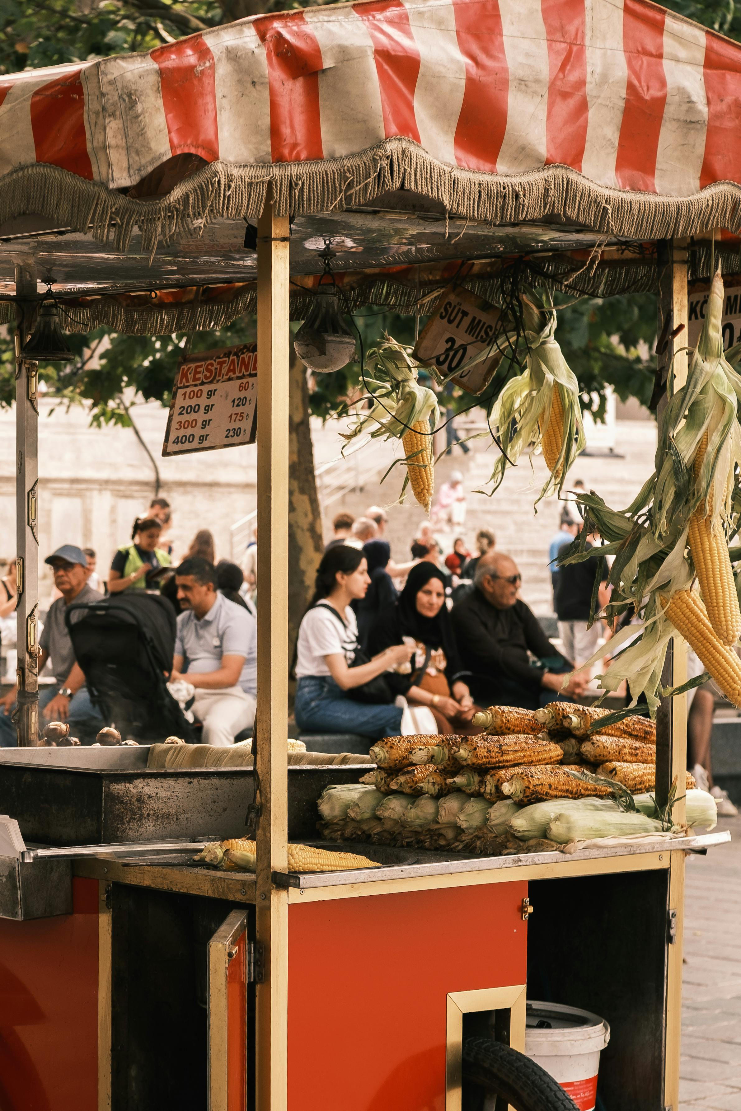 бесплатная Яркая тележка с уличной едой, где продают жареную кукурузу, расположена в оживленном городском районе, где много людей. Стоковое фото