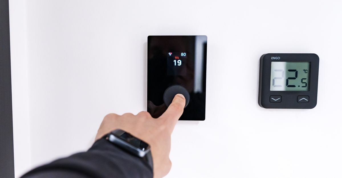 Hand stellt ein digitales Thermostat im Wohnraum ein