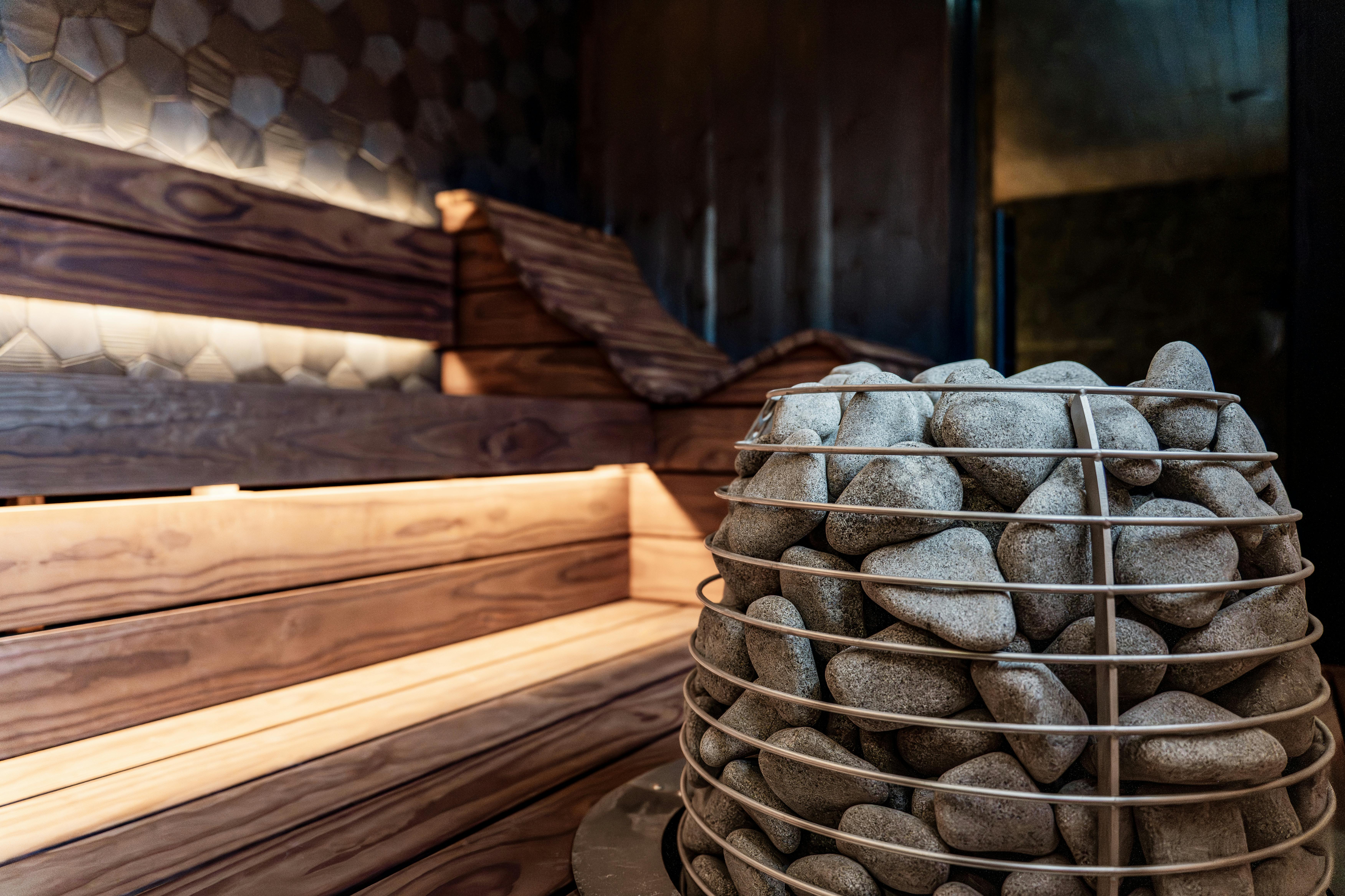 Sauna intérieur élégant avec bancs en bois, poêle en pierre et éclairage moderne.