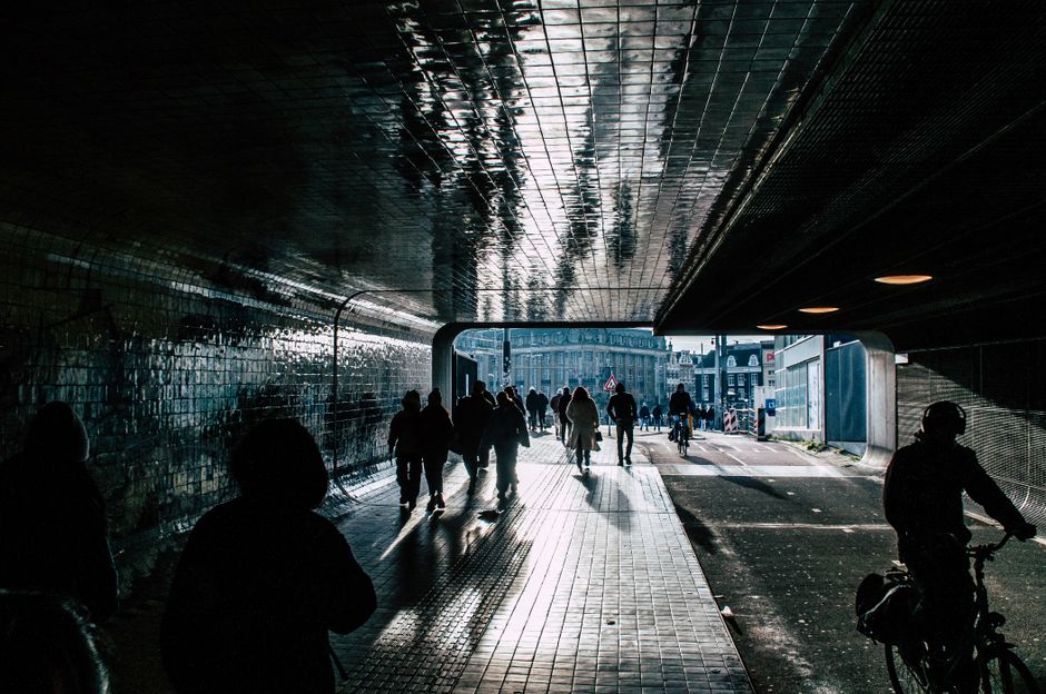 Urban scene with silhouettes of pedestrians and cyclists in a tunnel during day.