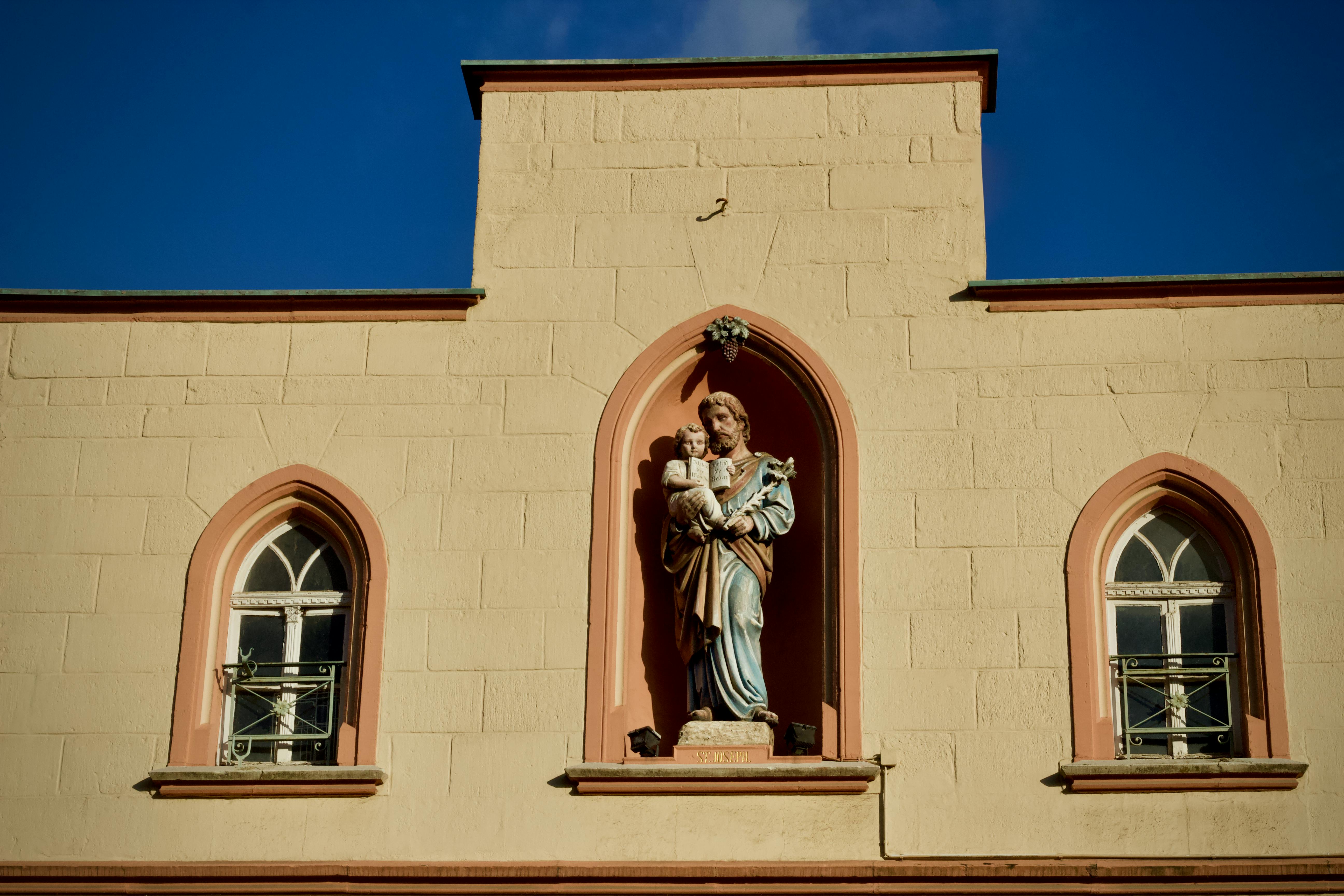 Miễn phí Một bức tượng thánh nhân bế một đứa trẻ trên mặt tiền của một tòa nhà lịch sử dưới bầu trời xanh trong vắt. Ảnh lưu trữ