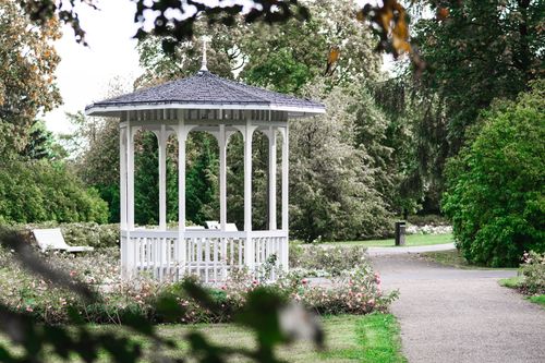 Free A picturesque white gazebo in a lush green park with surrounding flowers in Keila, Estonia, captured in summer. Stock Photo