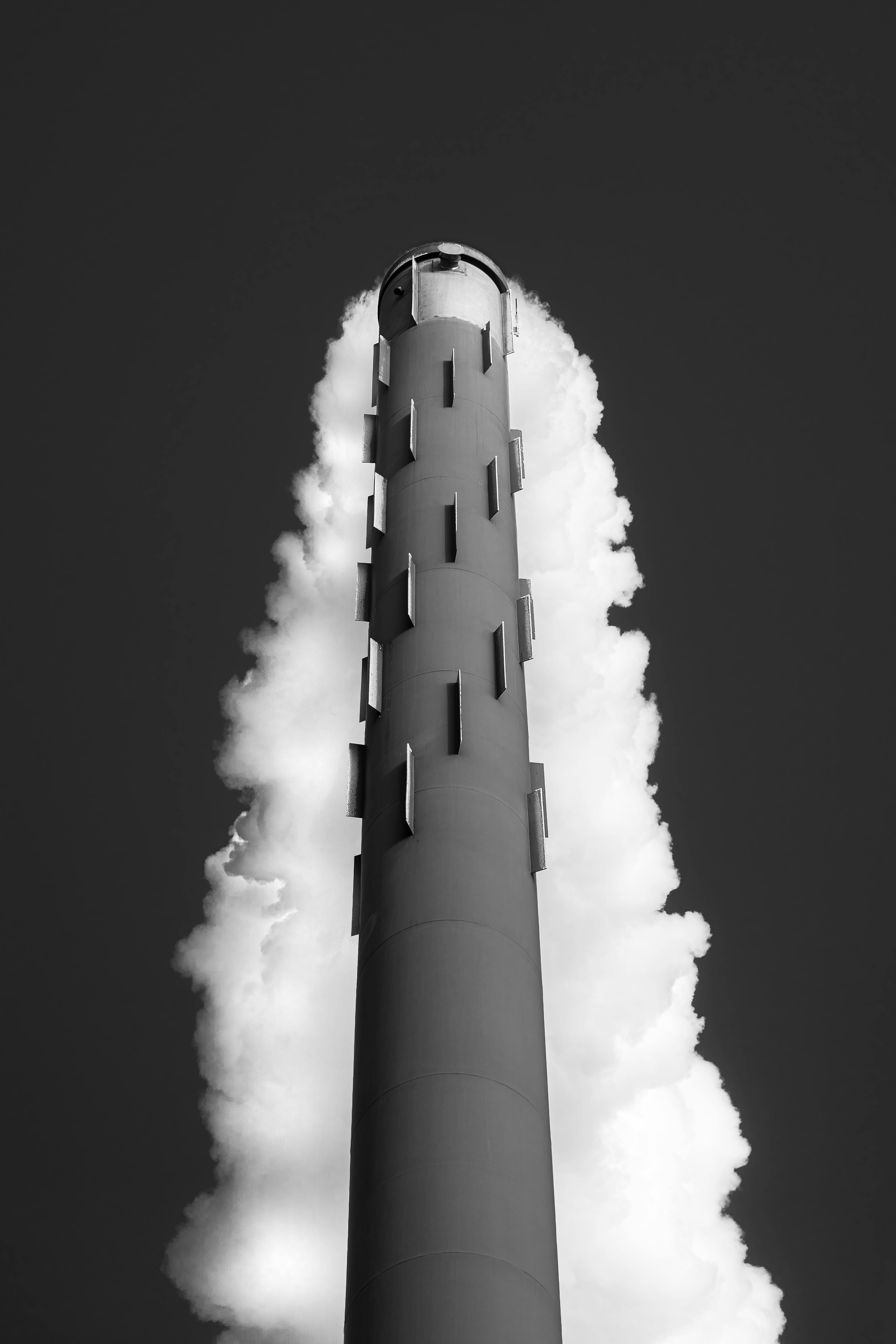 gratis Zwart-witfoto van een industriële schoorsteen die rook tegen de hemel uitblaast, waardoor een scherpe verticale compositie ontstaat. Stockfoto