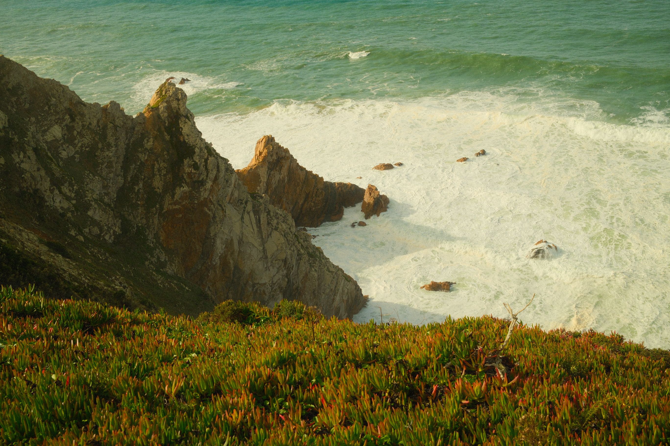 Sweeping view of rugged cliffs meeting crashing ocean waves in Colares, Portugal.