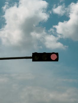 Red traffic light hanging in front of a cloudy sky, signaling stop.