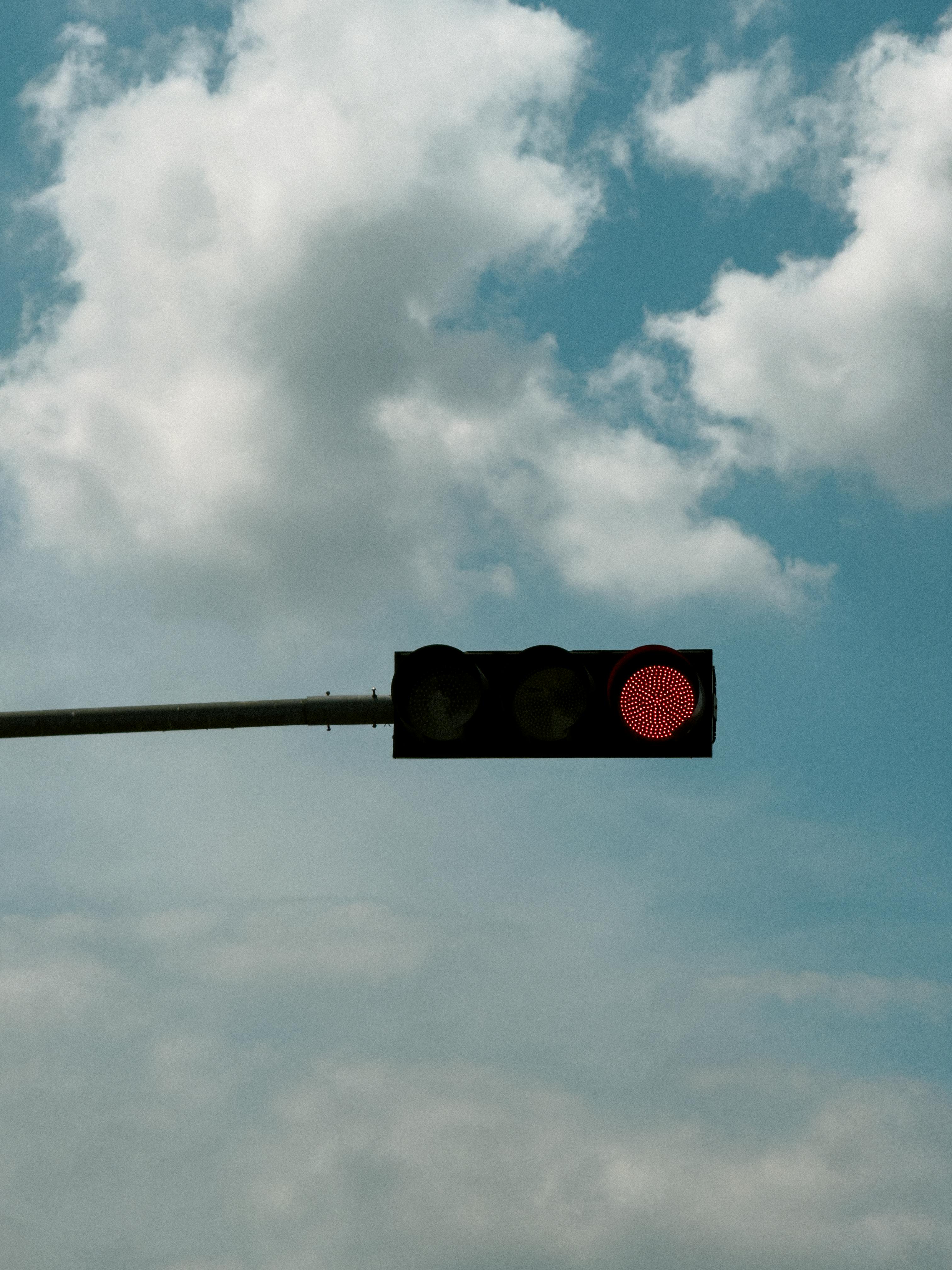 Free Red traffic light hanging in front of a cloudy sky, signaling stop. Stock Photo