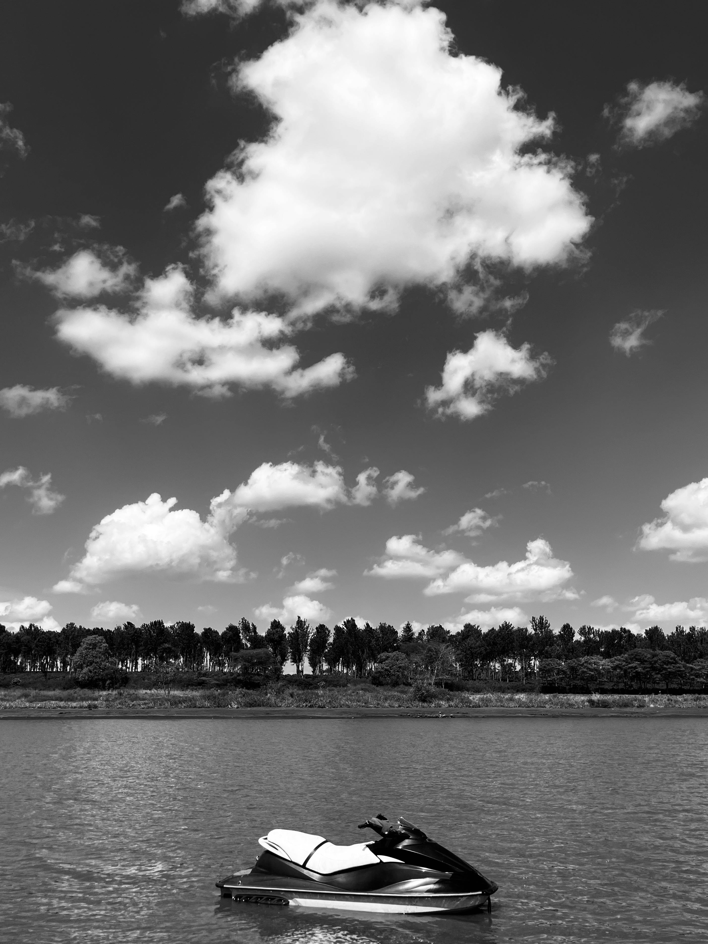 grátis Uma impressionante foto em preto e branco de um jet ski em um lago tranquilo com uma paisagem de nuvens dramática. Foto profissional